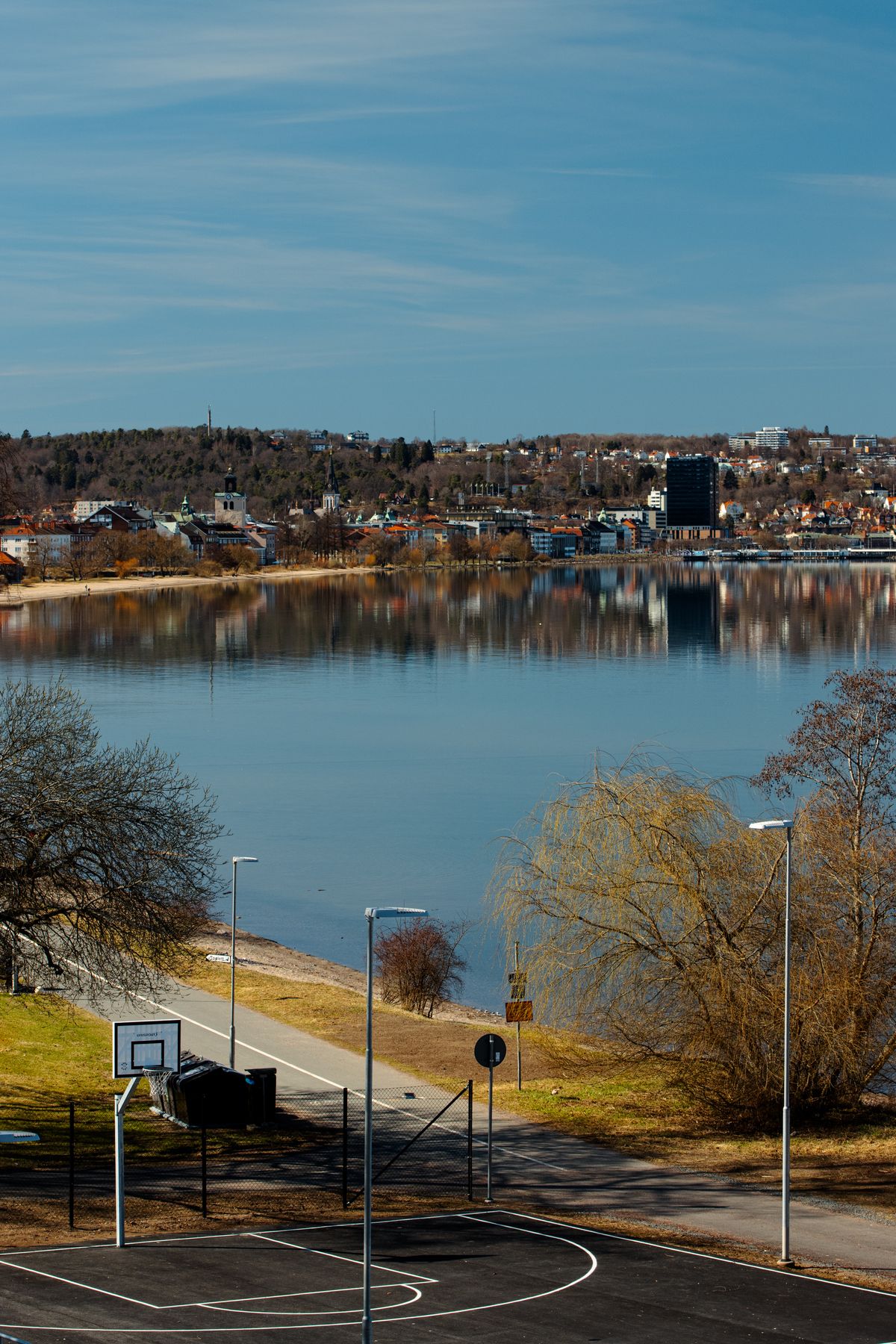 A calm lake in Jönköping, Sweden, reflecting pine trees and a golden summer sky in still water