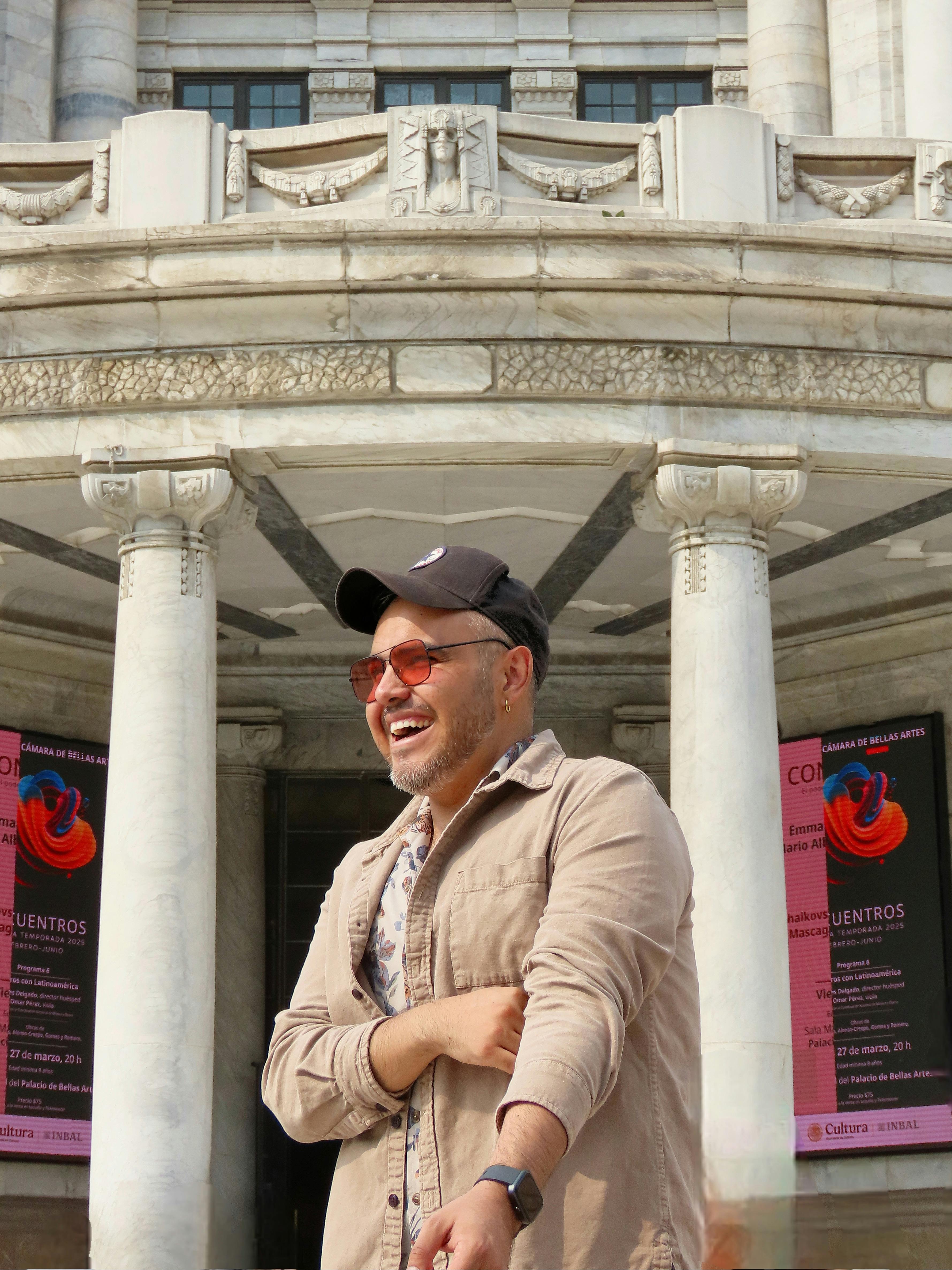Man smiling in front of Palacio de Bellas Artes in daylight, adds joy.