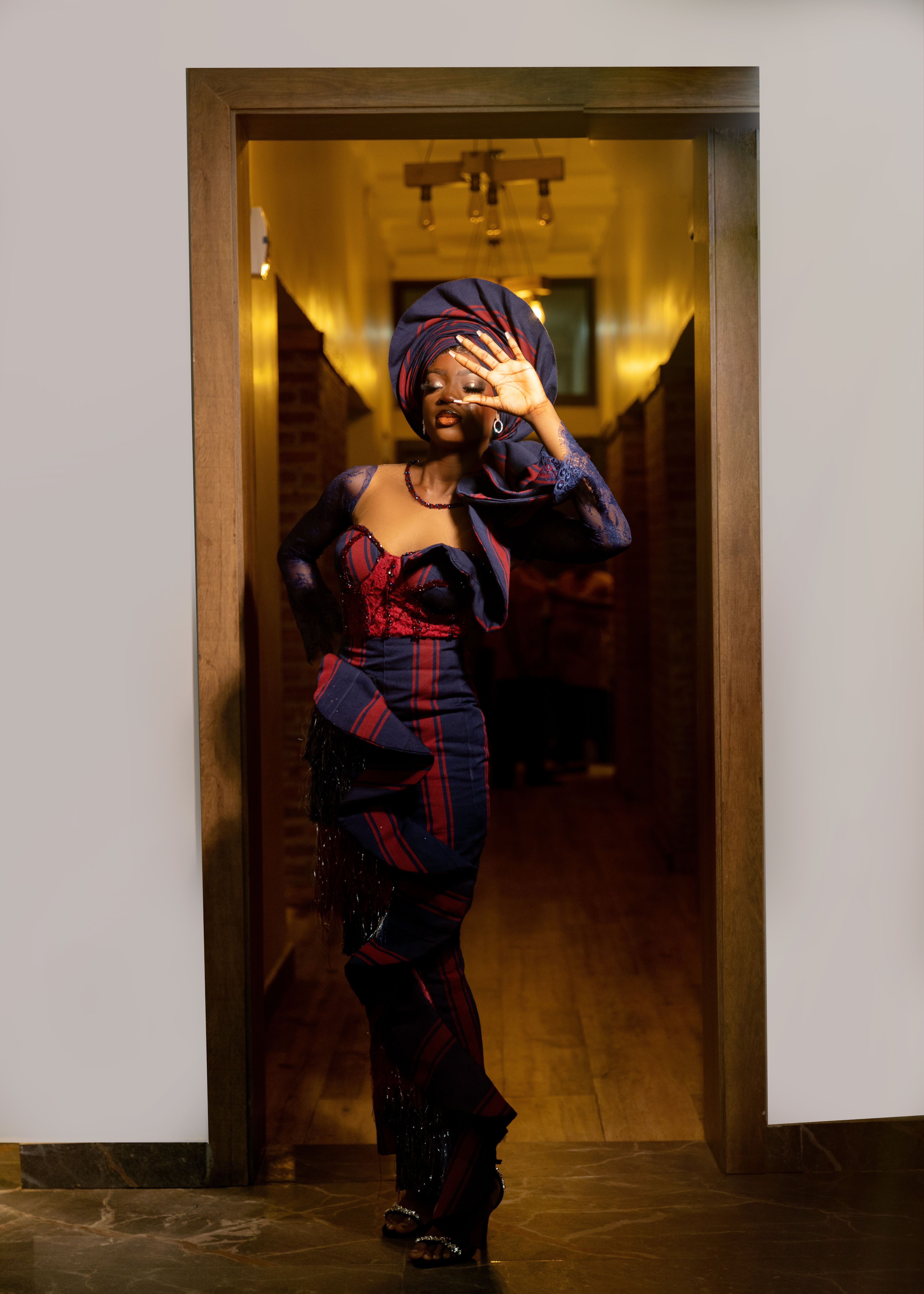 Sophisticated woman in vibrant traditional fashion in a warmly lit hallway.