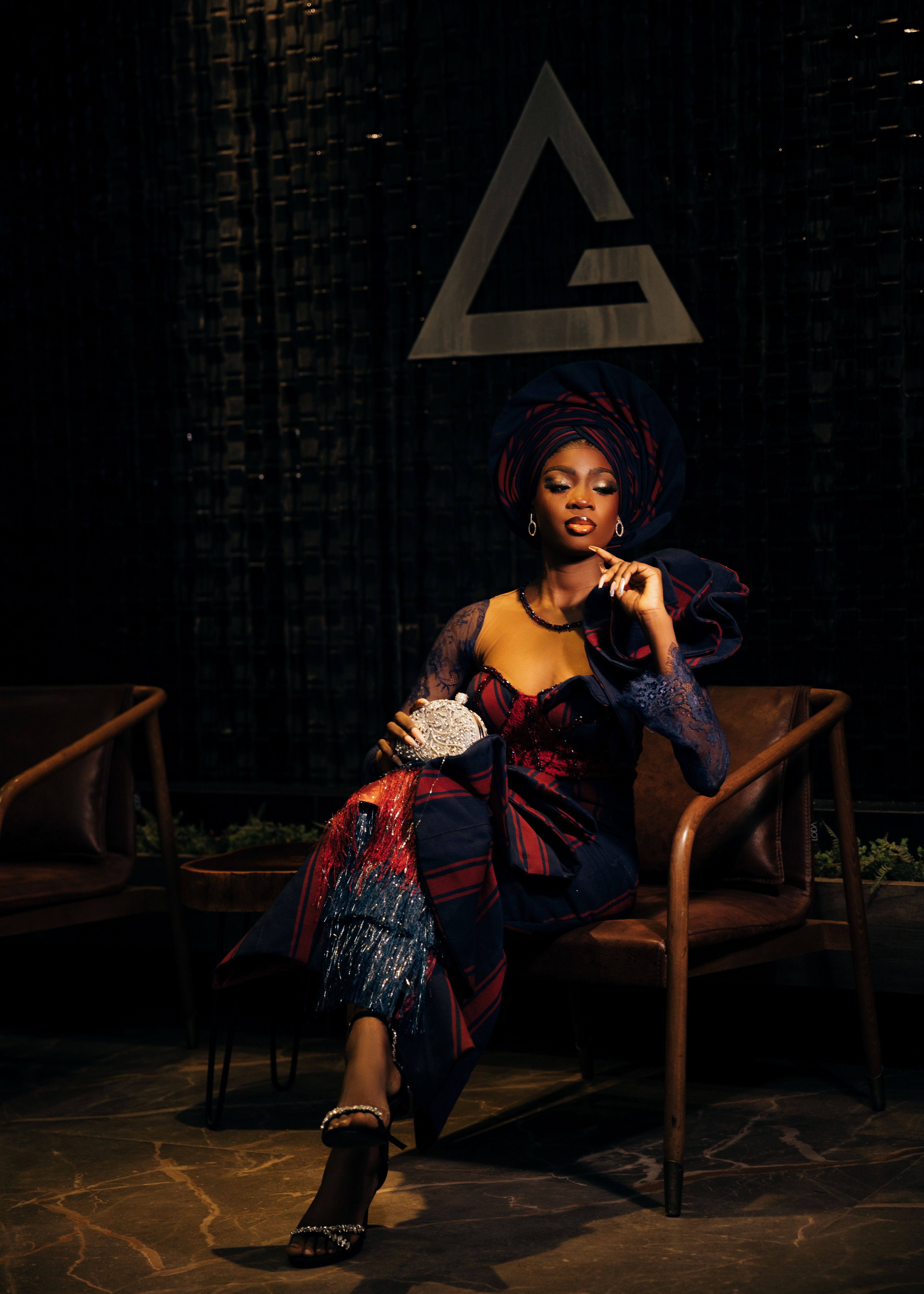 Sophisticated woman in traditional outfit seated in dimly lit room holding a clutch.