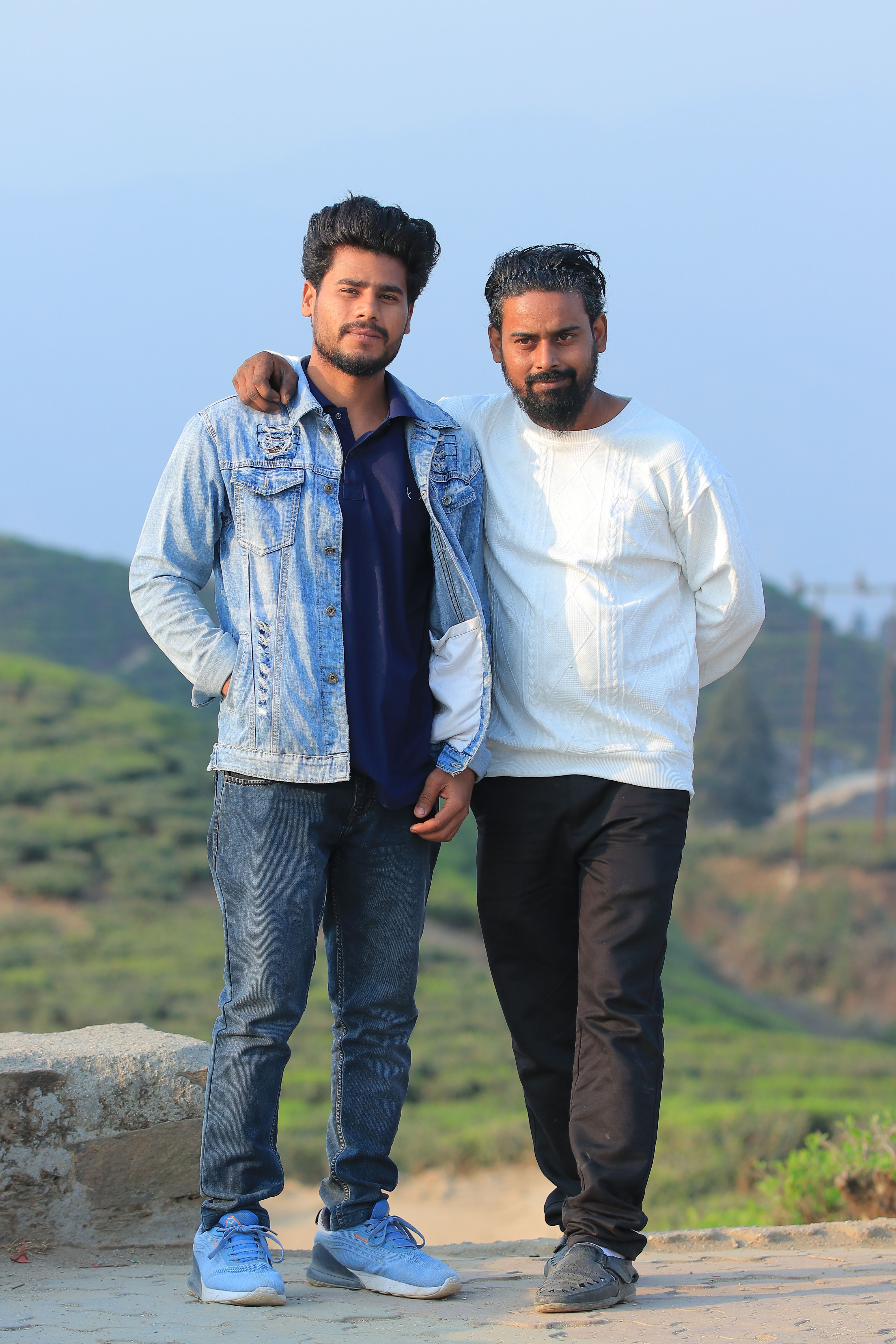 Two South Asian men posing outdoors with scenic background.