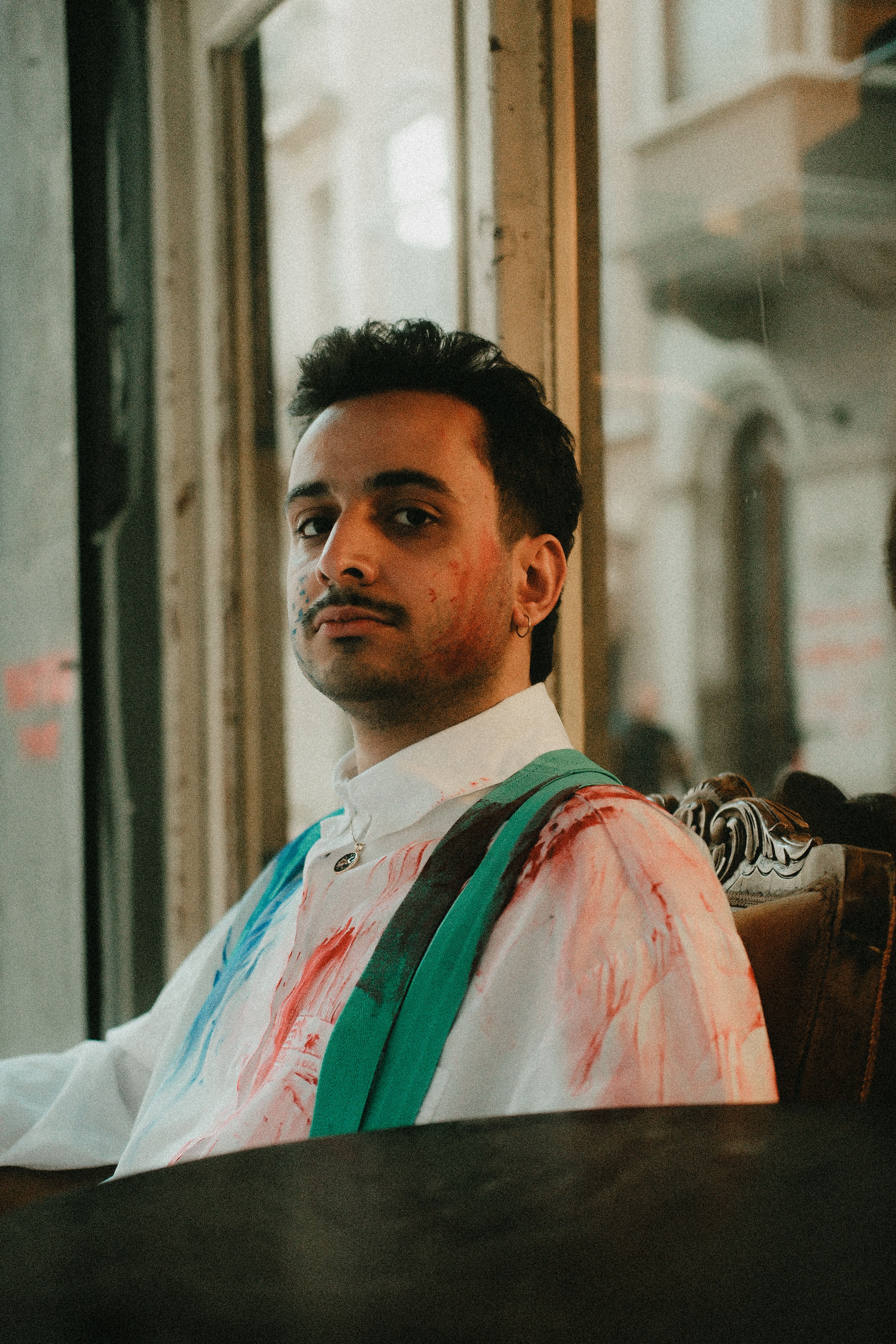 Young man with colorful shirt sitting pensively by a vintage window, creating a moody ambiance.