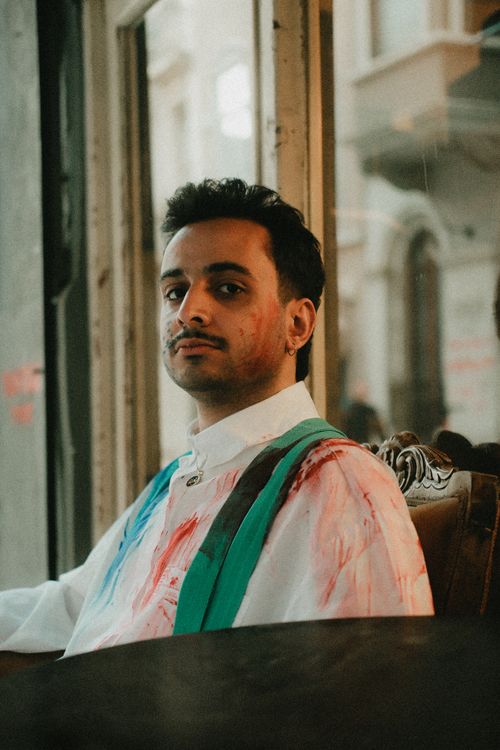 Free Young man with colorful shirt sitting pensively by a vintage window, creating a moody ambiance. Stock Photo