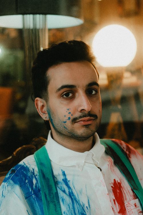 Free A man with paint splashes on his face and shirt in a creative indoor setting. Stock Photo