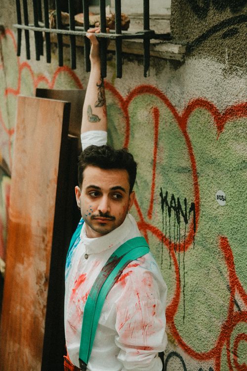 Free Young man in white shirt with paint splashes, posing against graffiti wall. Stock Photo