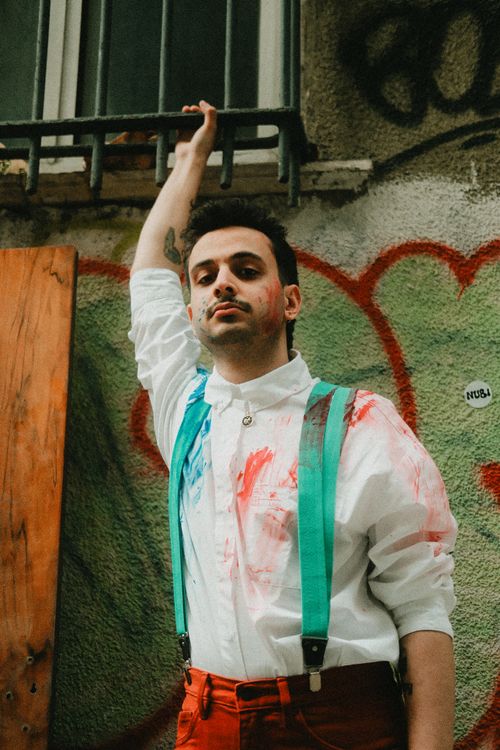 Free Man with painted shirt and suspenders posing against graffiti wall outdoors. Stock Photo