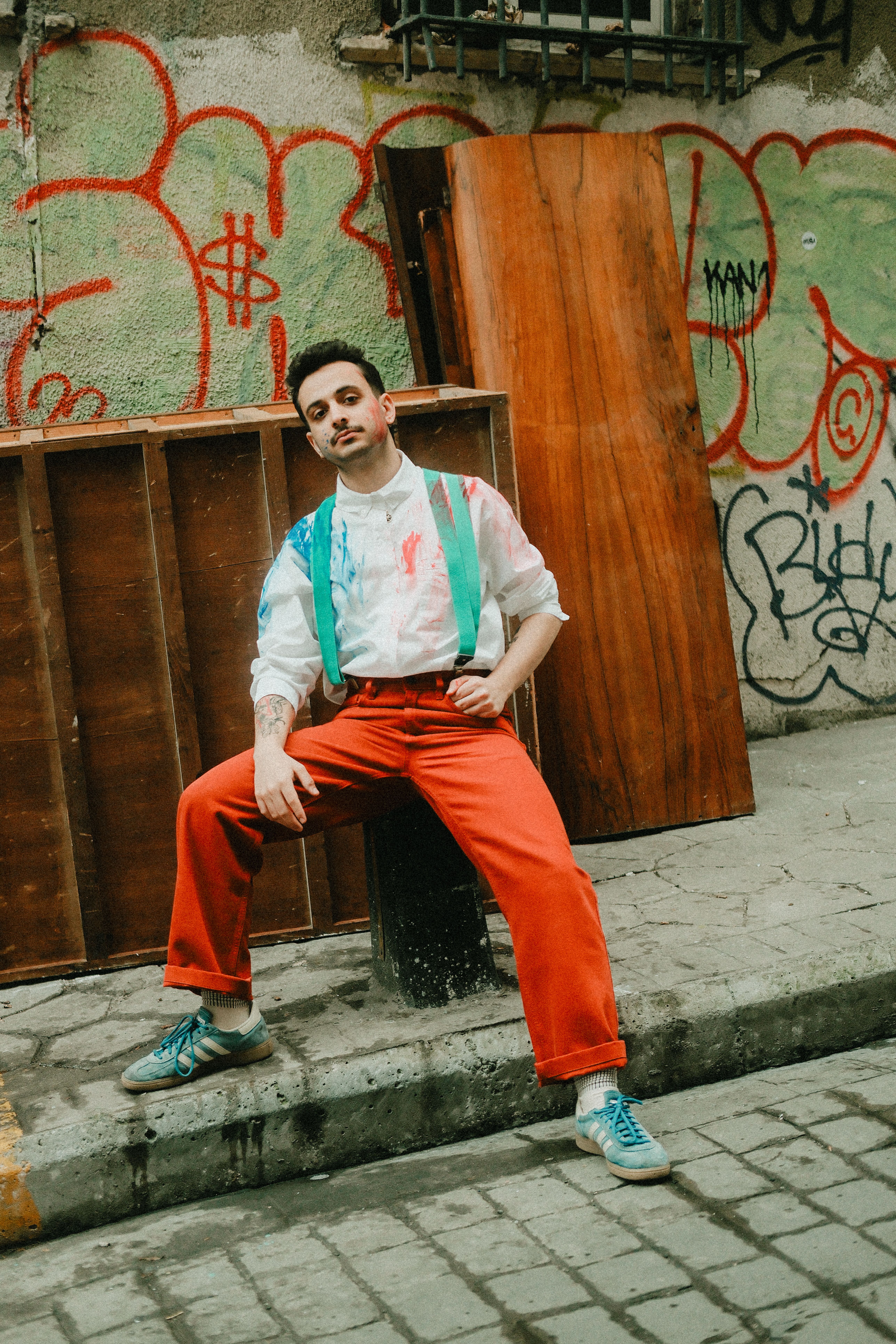 Man in vibrant outfit poses confidently on a graffiti-adorned urban alley.