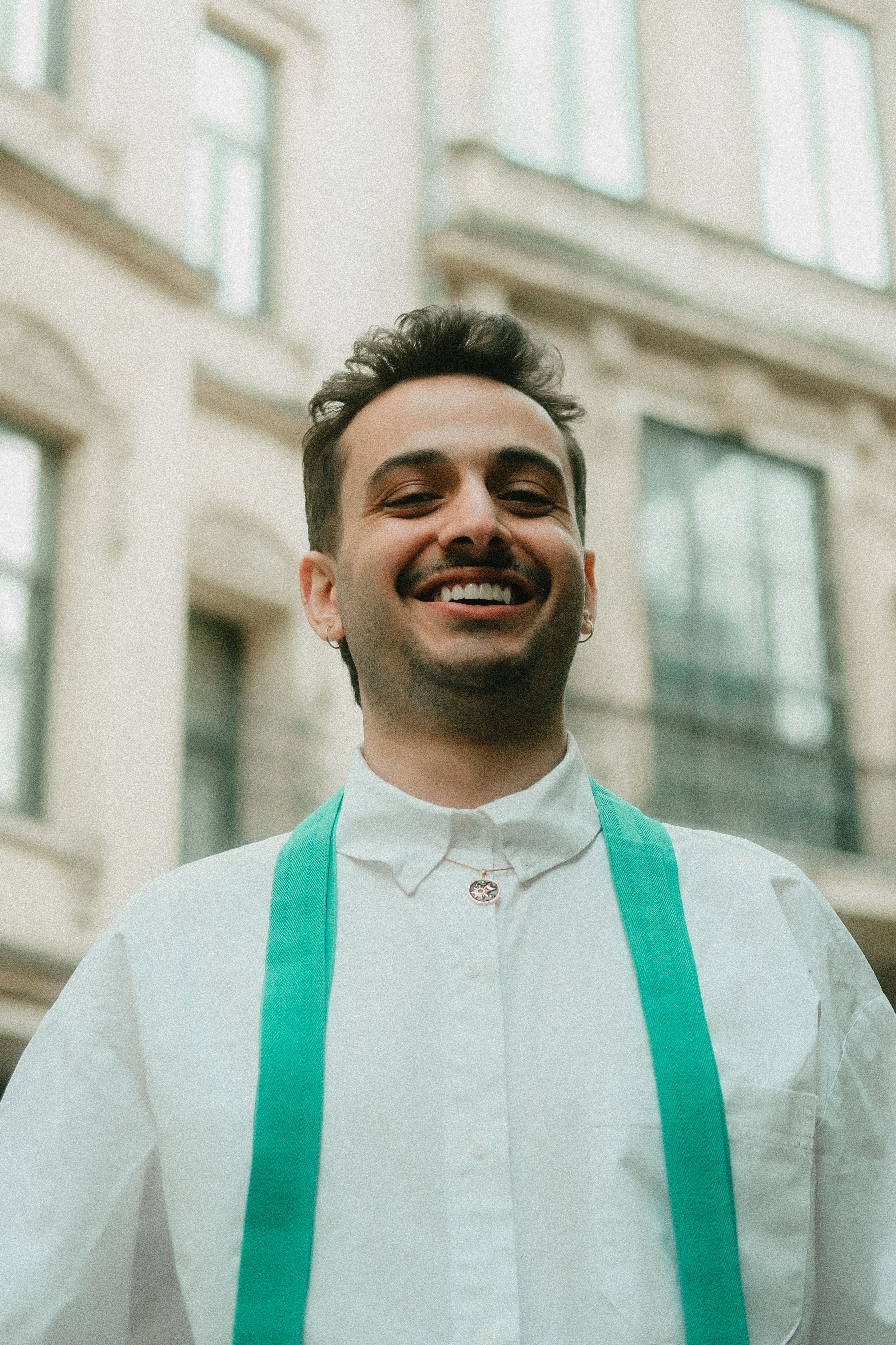 Happy man with green suspenders smiles in an urban outdoor setting.