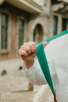 Close-up of a person holding a green suspender against an outdoor urban backdrop.