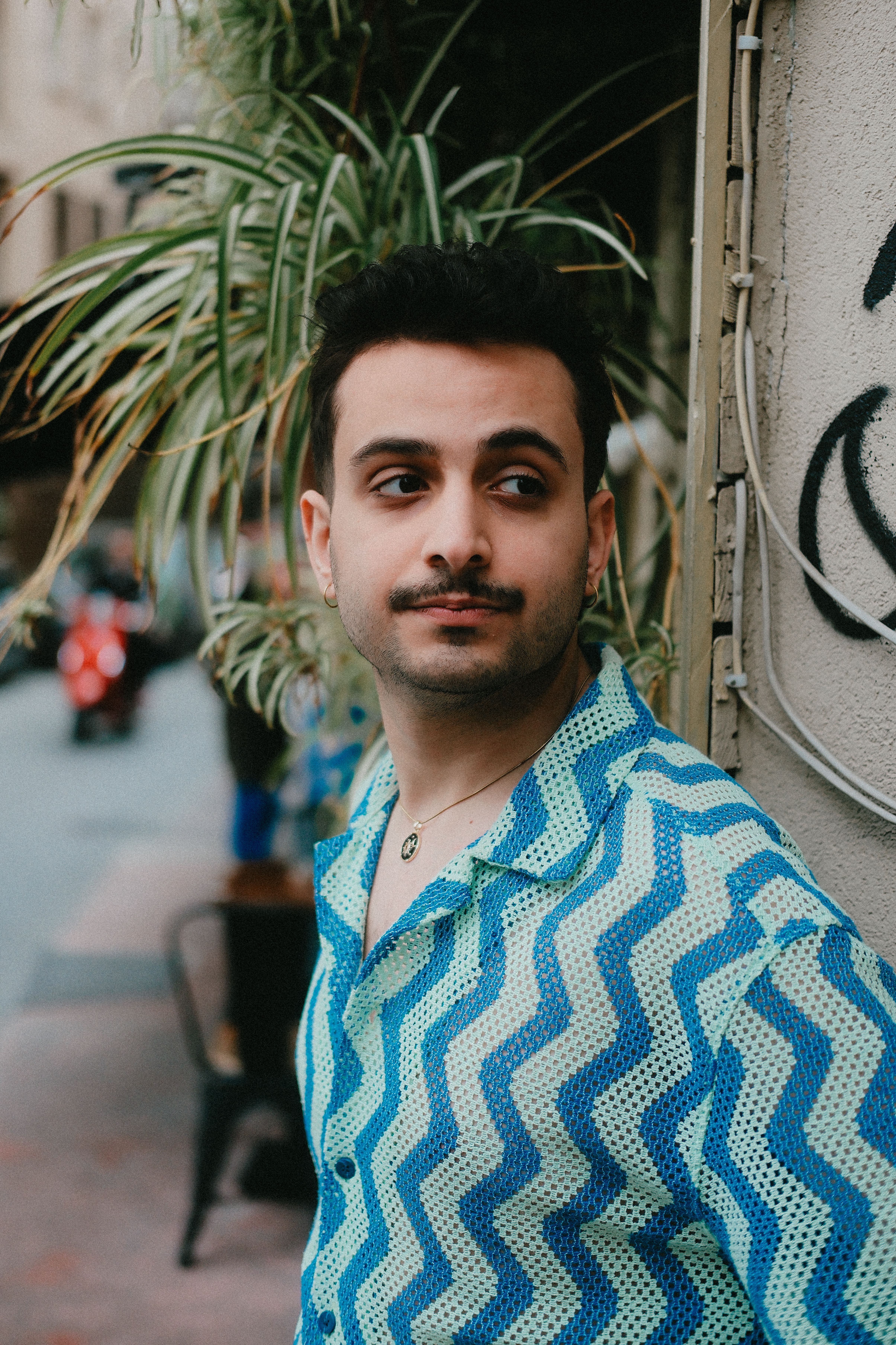 Portrait of a man in a blue patterned shirt standing on an urban street, looking away.