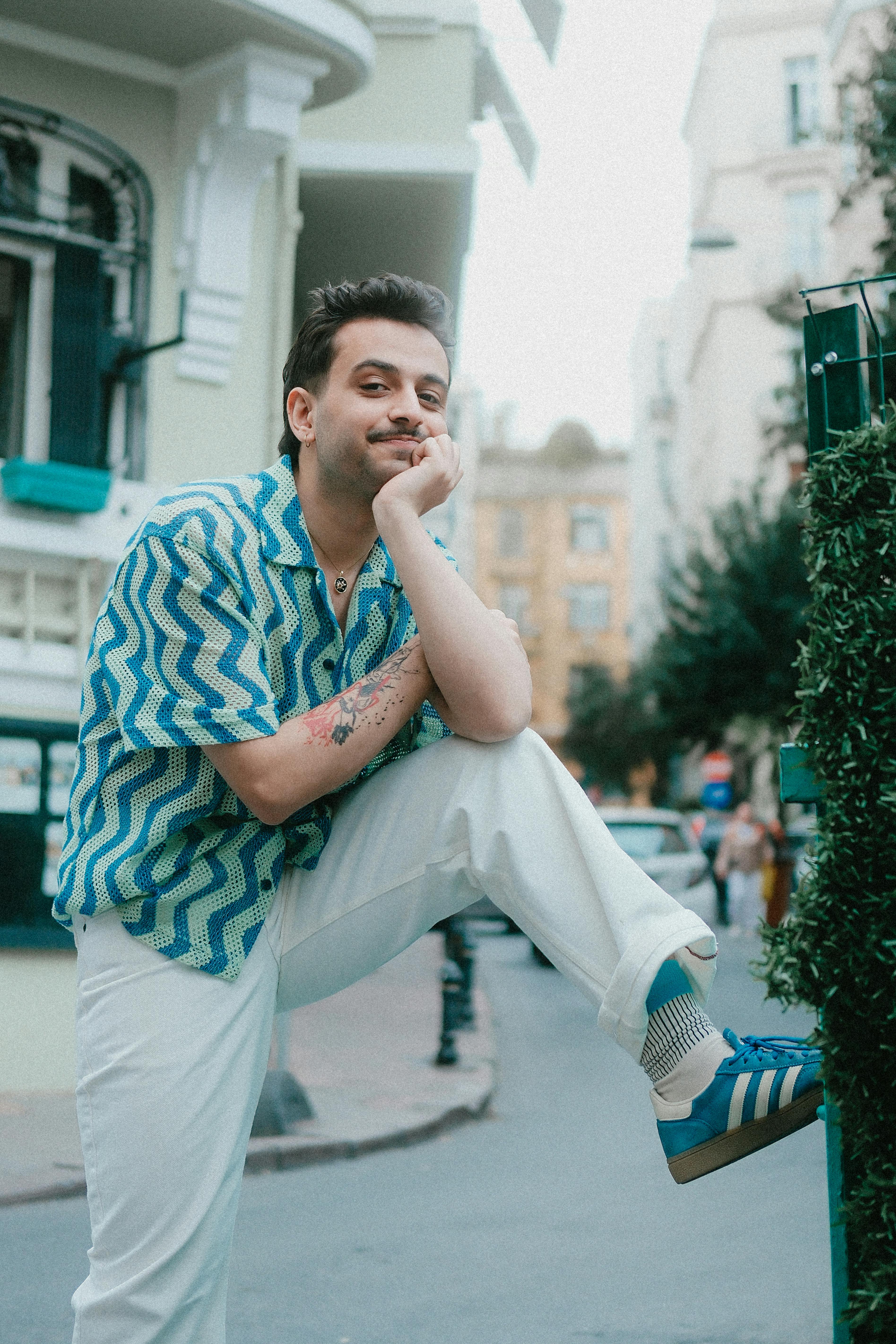 Casually dressed man in zigzag shirt poses confidently on a city street corner, showcasing summer style.