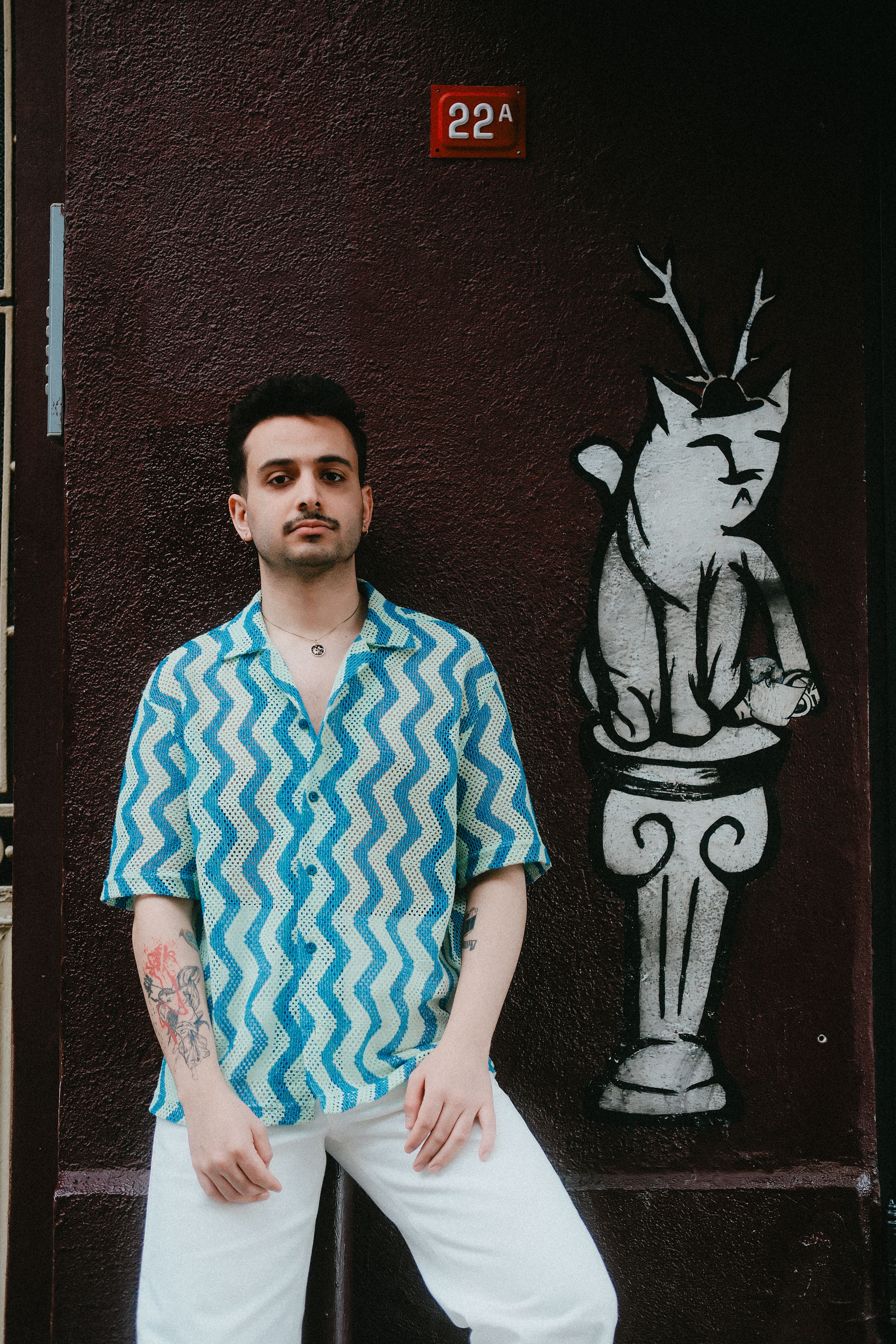 Stylish young man poses in front of a whimsical street art mural, adding urban flair.