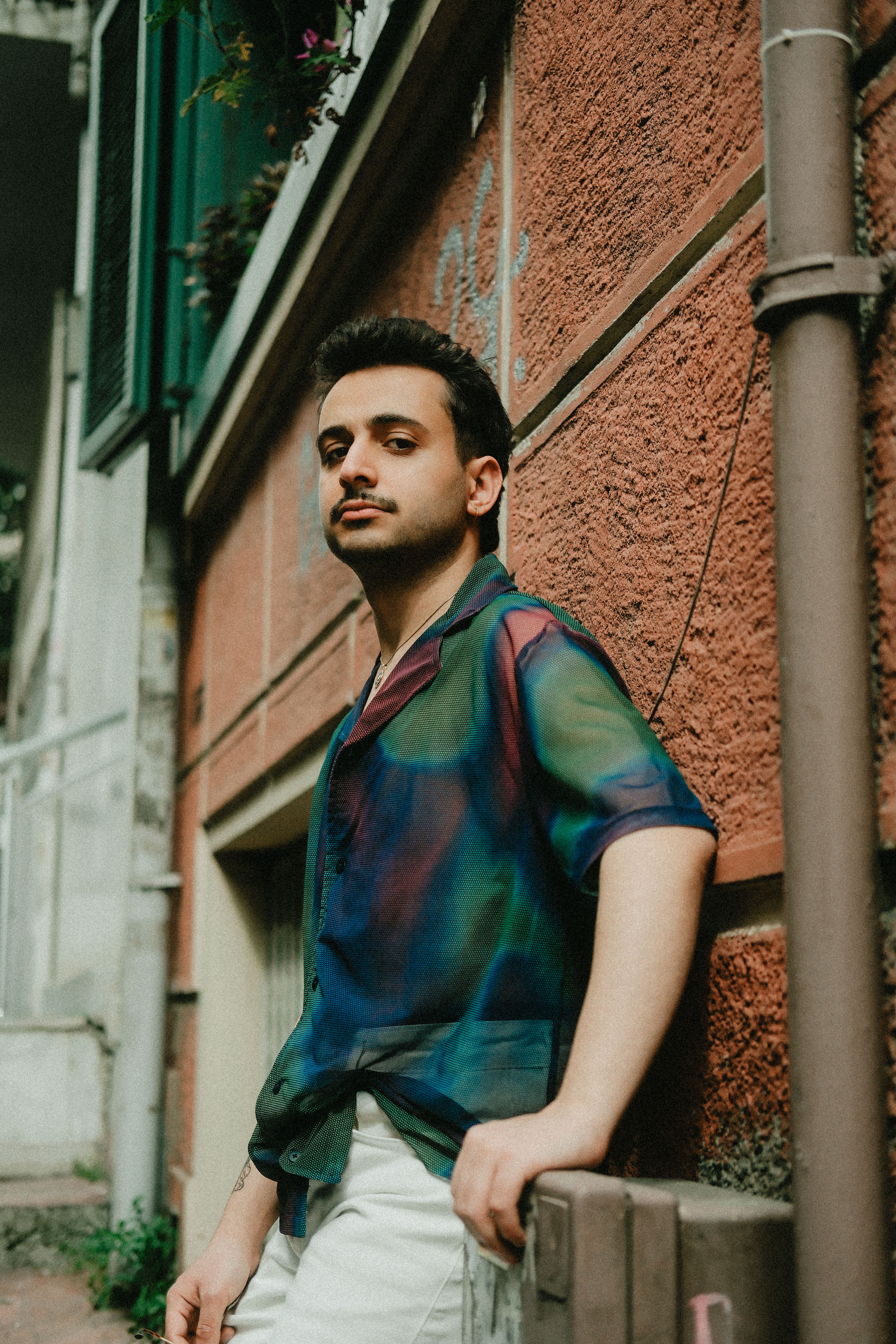 Stylish man in colorful shirt poses against urban wall outdoors.