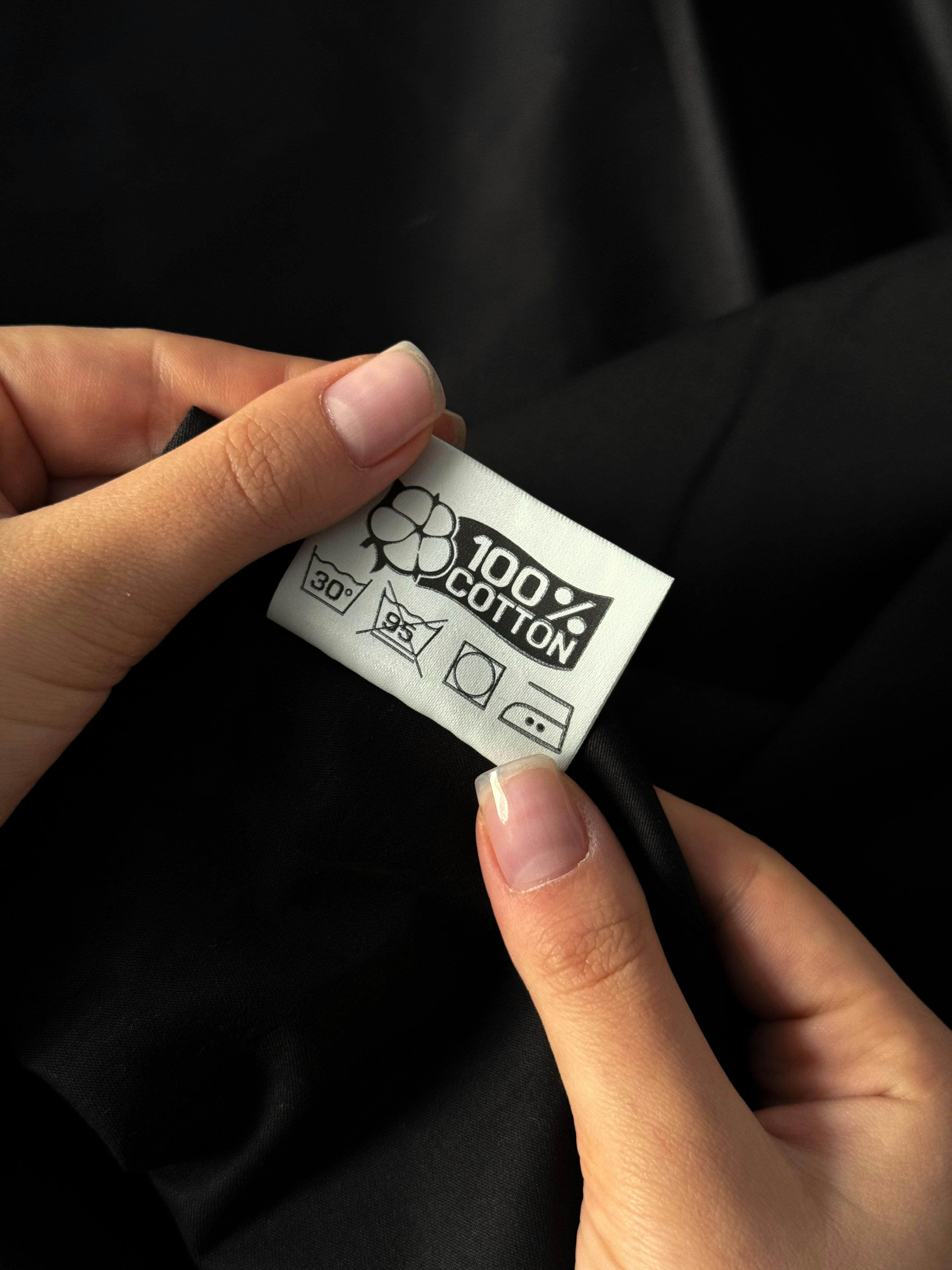 Hands of a woman examining a 100% cotton tag on clothing against a dark background.