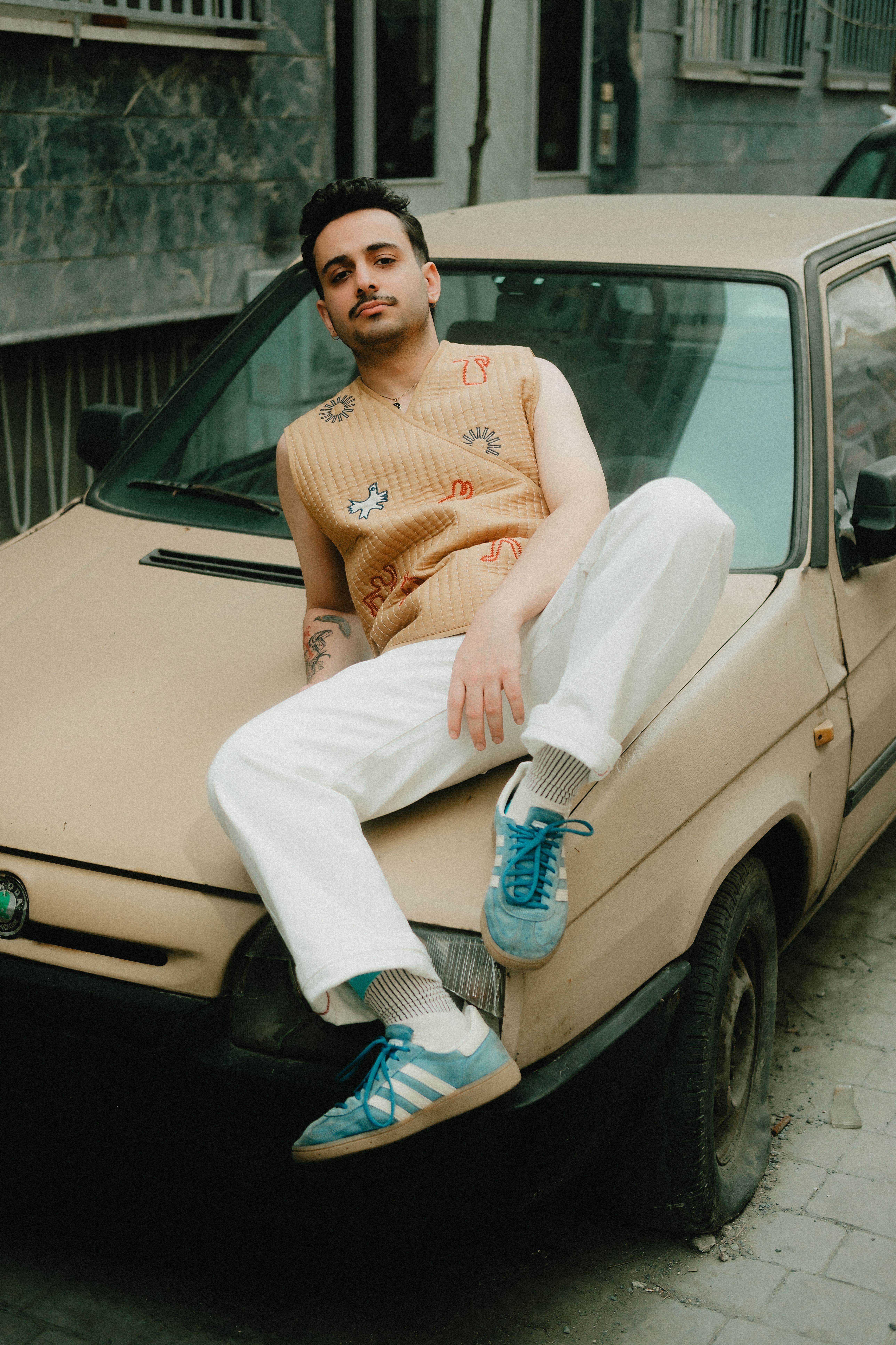 Fashionable young man with casual style poses on a vintage car outdoors.