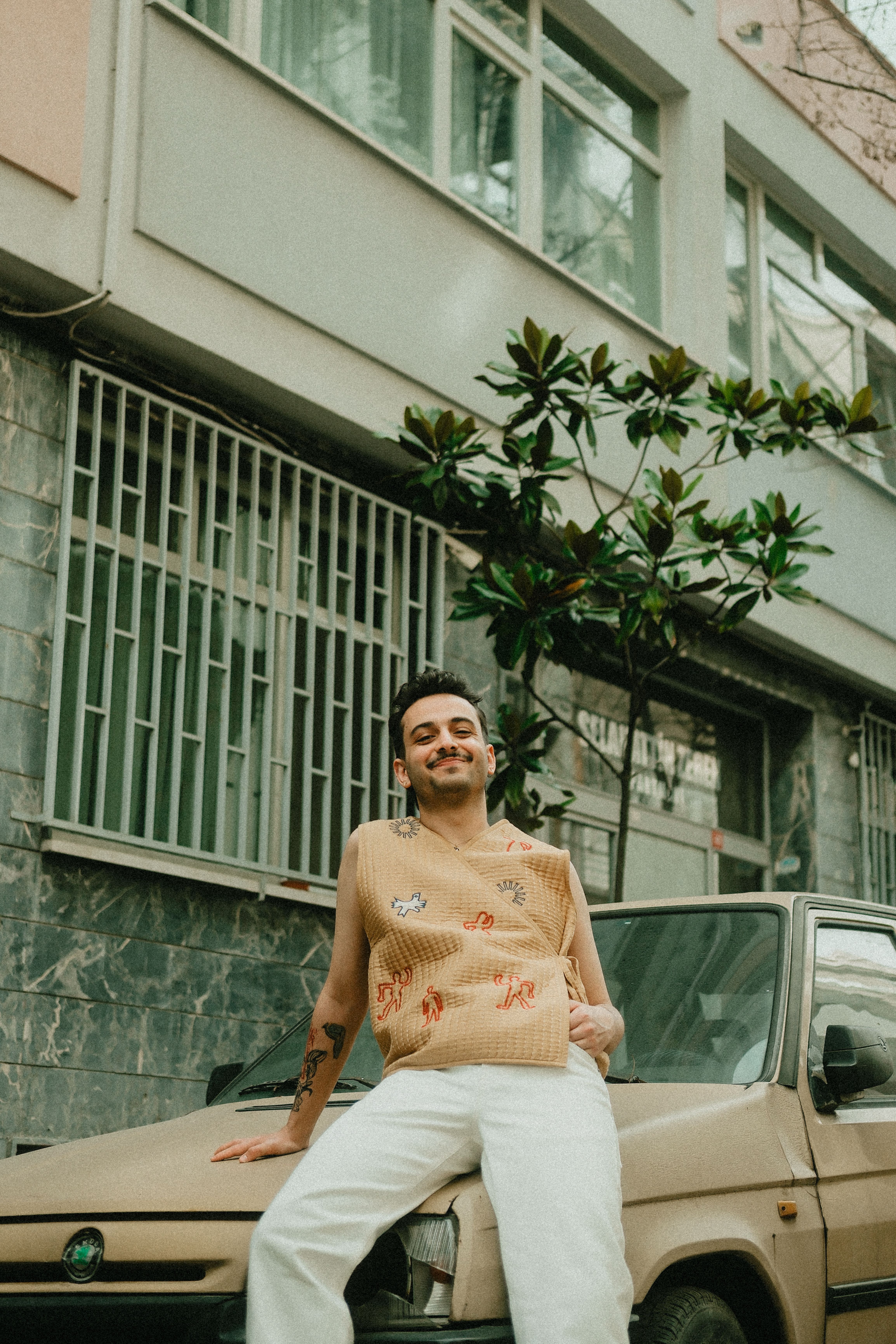 Stylish man in casual attire posing on an old car in an urban setting. Outdoors relaxed scene.