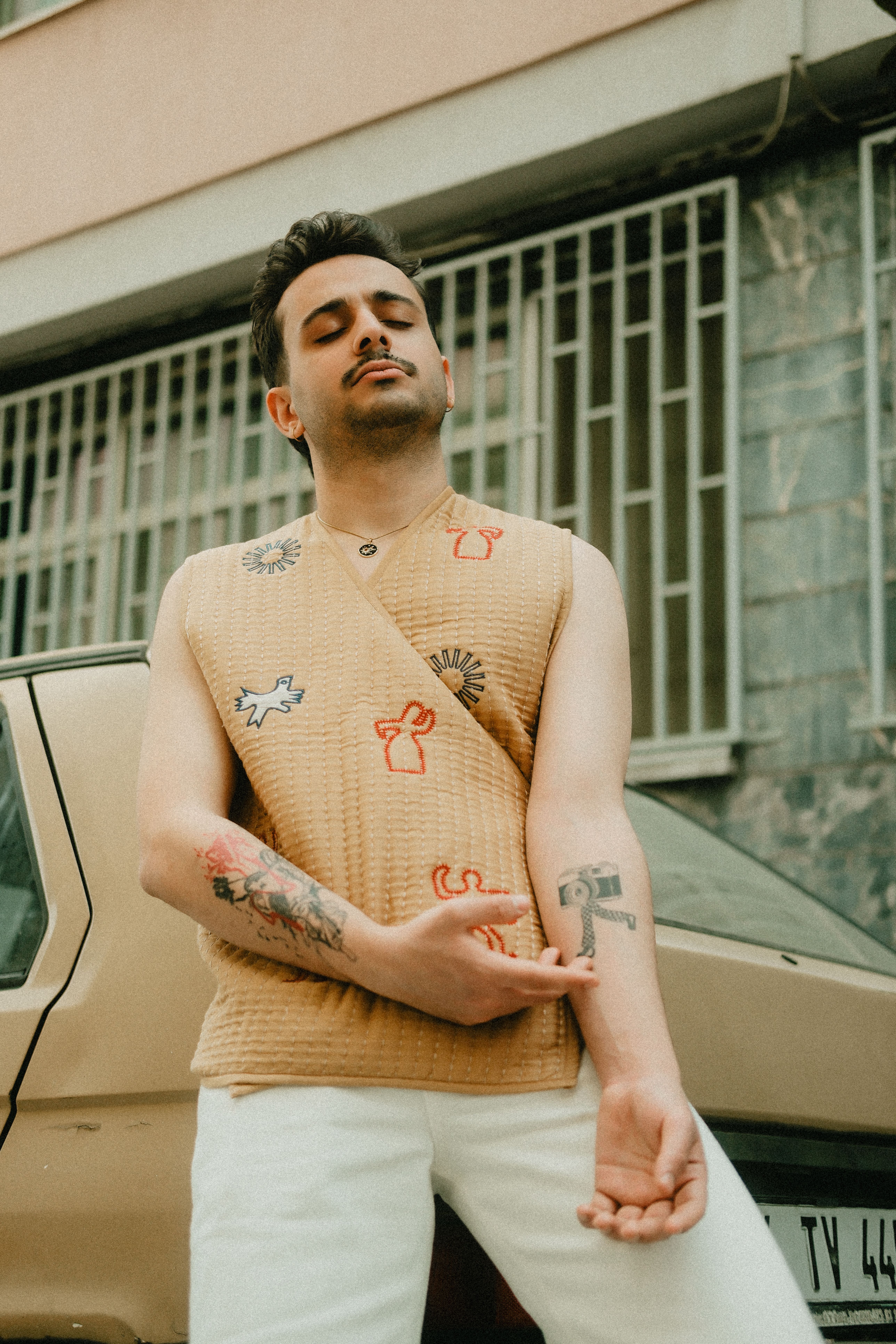 Stylish young man showing tattoos, posing near a car outdoors.