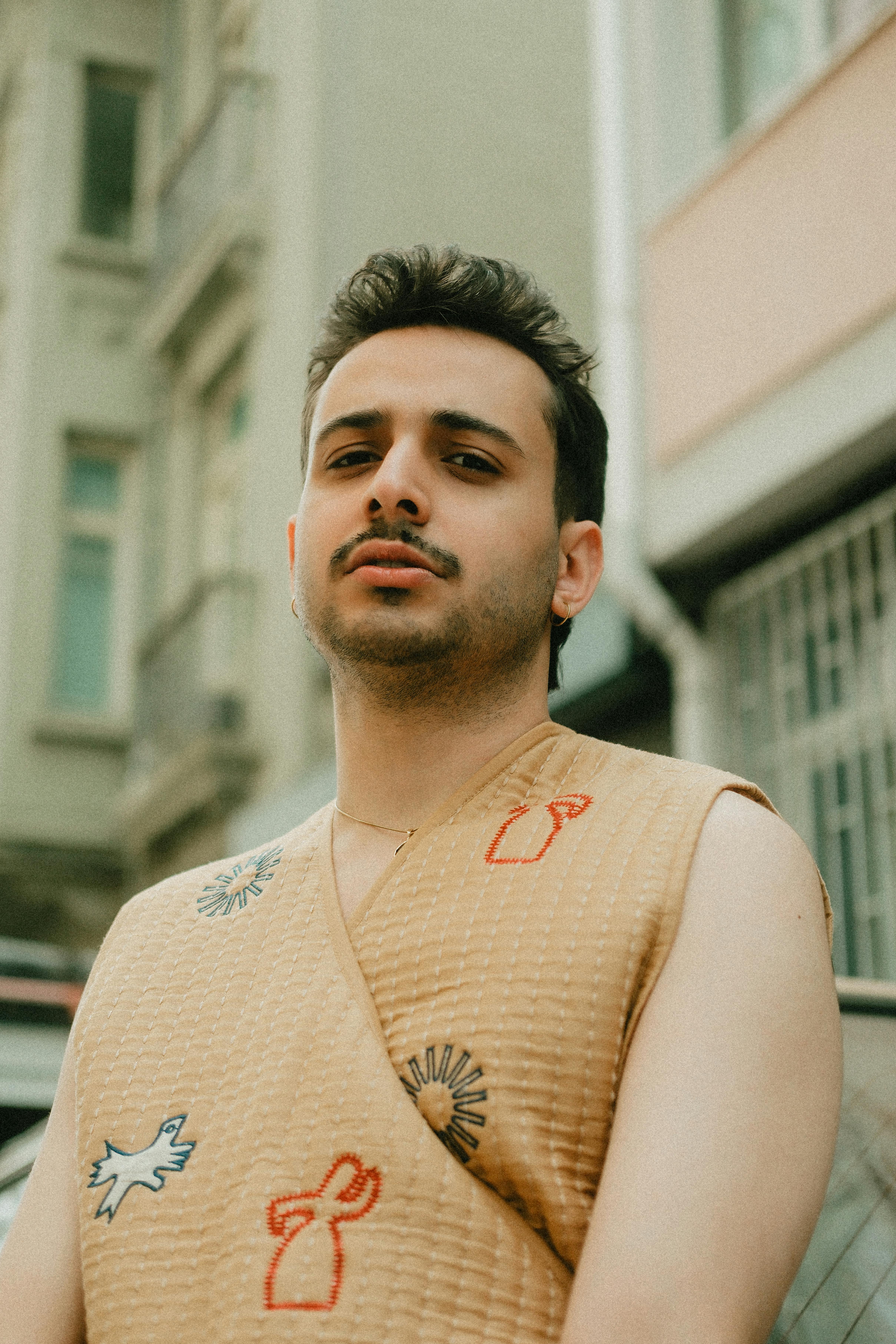 Stylish man wearing embroidered vest, posing confidently outside in urban setting.