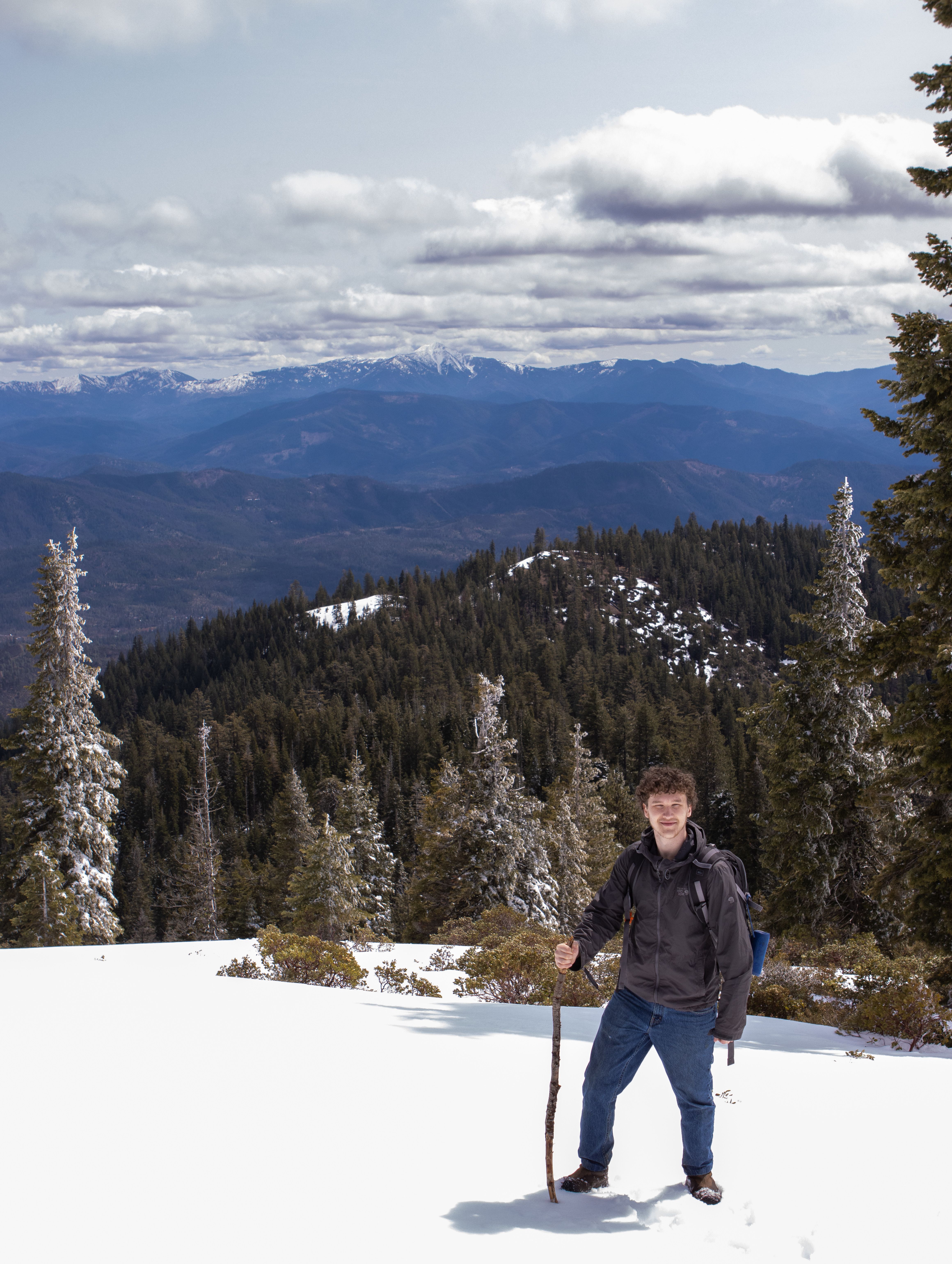 A lone hiker stands in snowy landscape with distant mountain views in Junction City, CA.