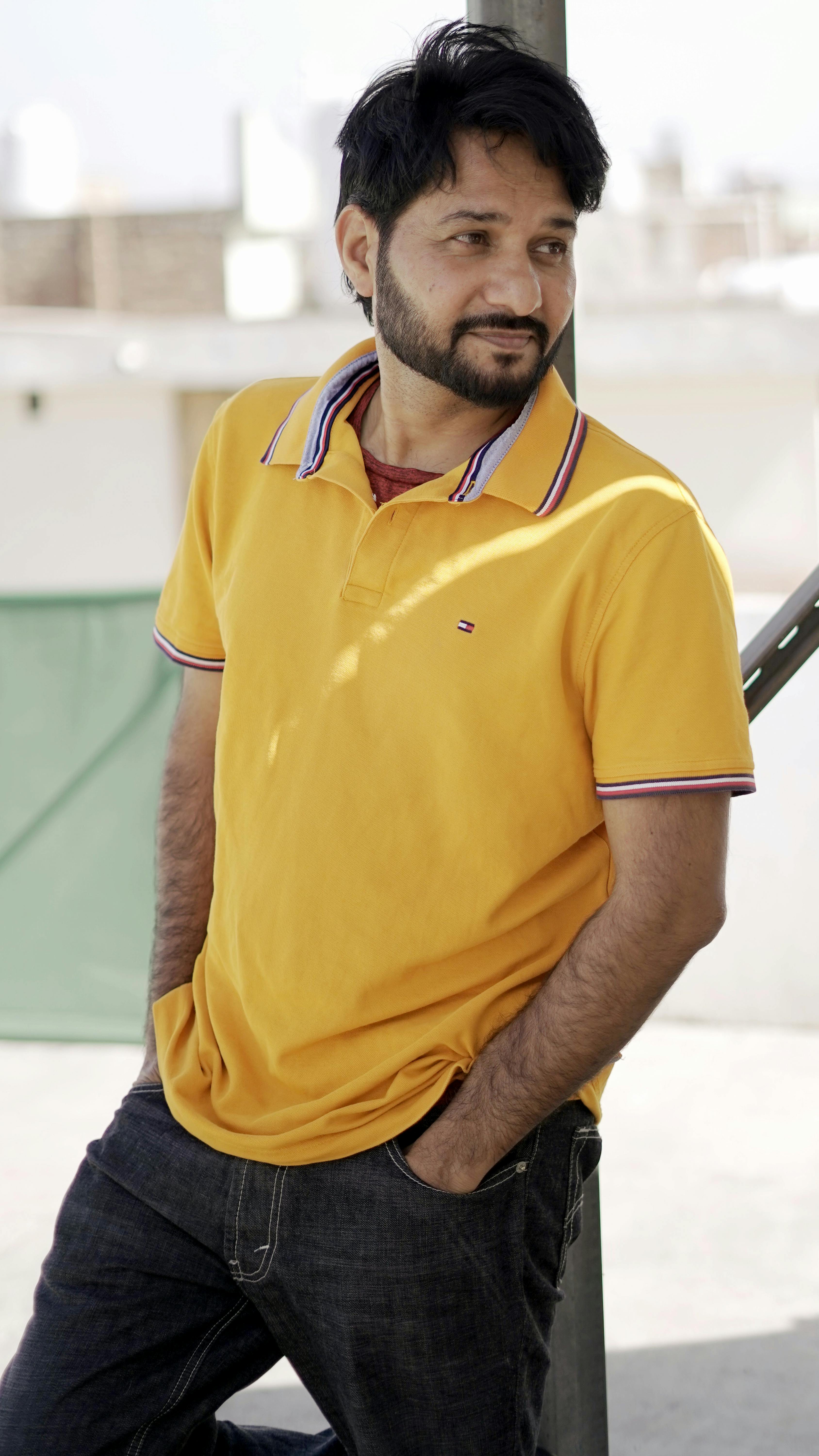 Man in yellow polo shirt casually posing outdoors on a sunny day.