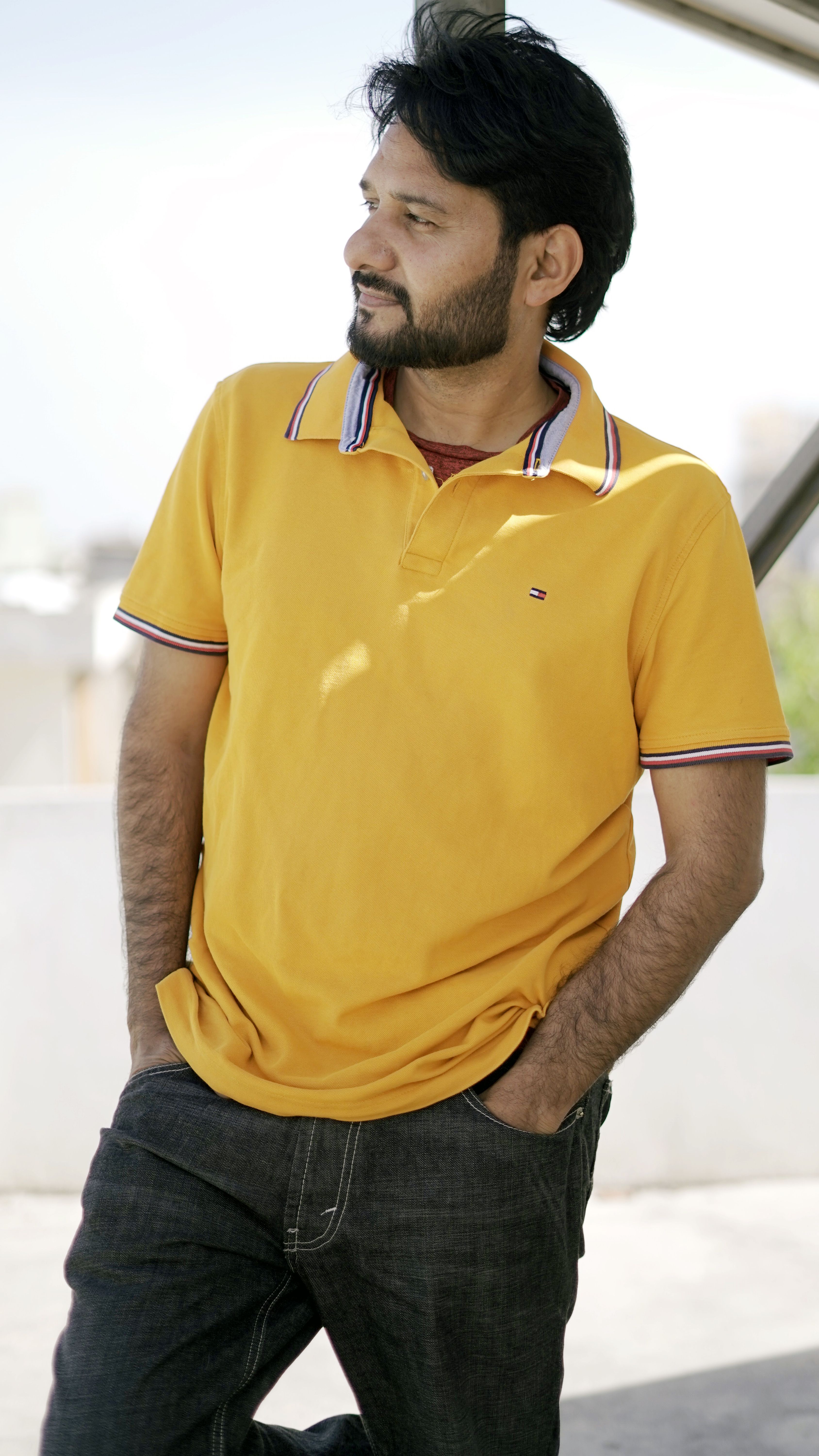 Portrait of an adult man in a yellow polo shirt standing outdoors, looking contemplative and relaxed.