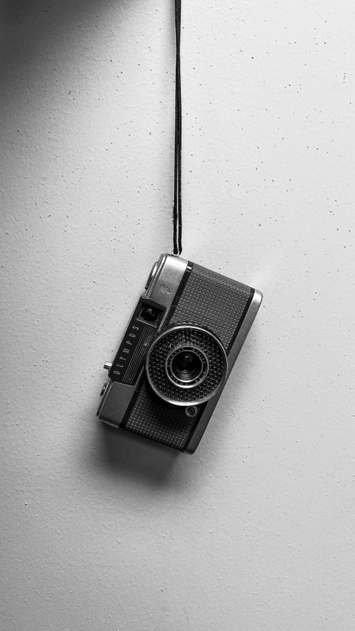 Free Black and white photo of a vintage film camera hanging against a white background. Stock Photo