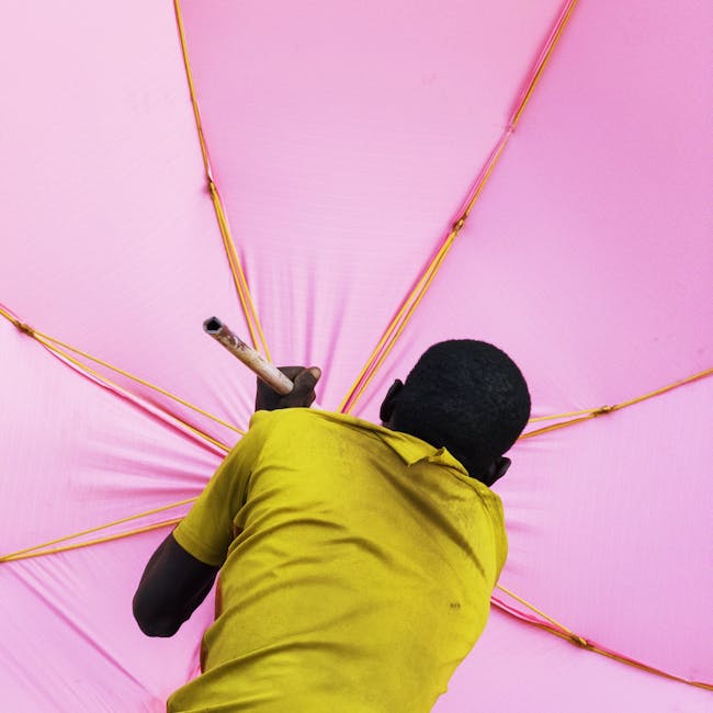 A man wearing a yellow shirt repairs a large pink umbrella in Kano, Nigeria