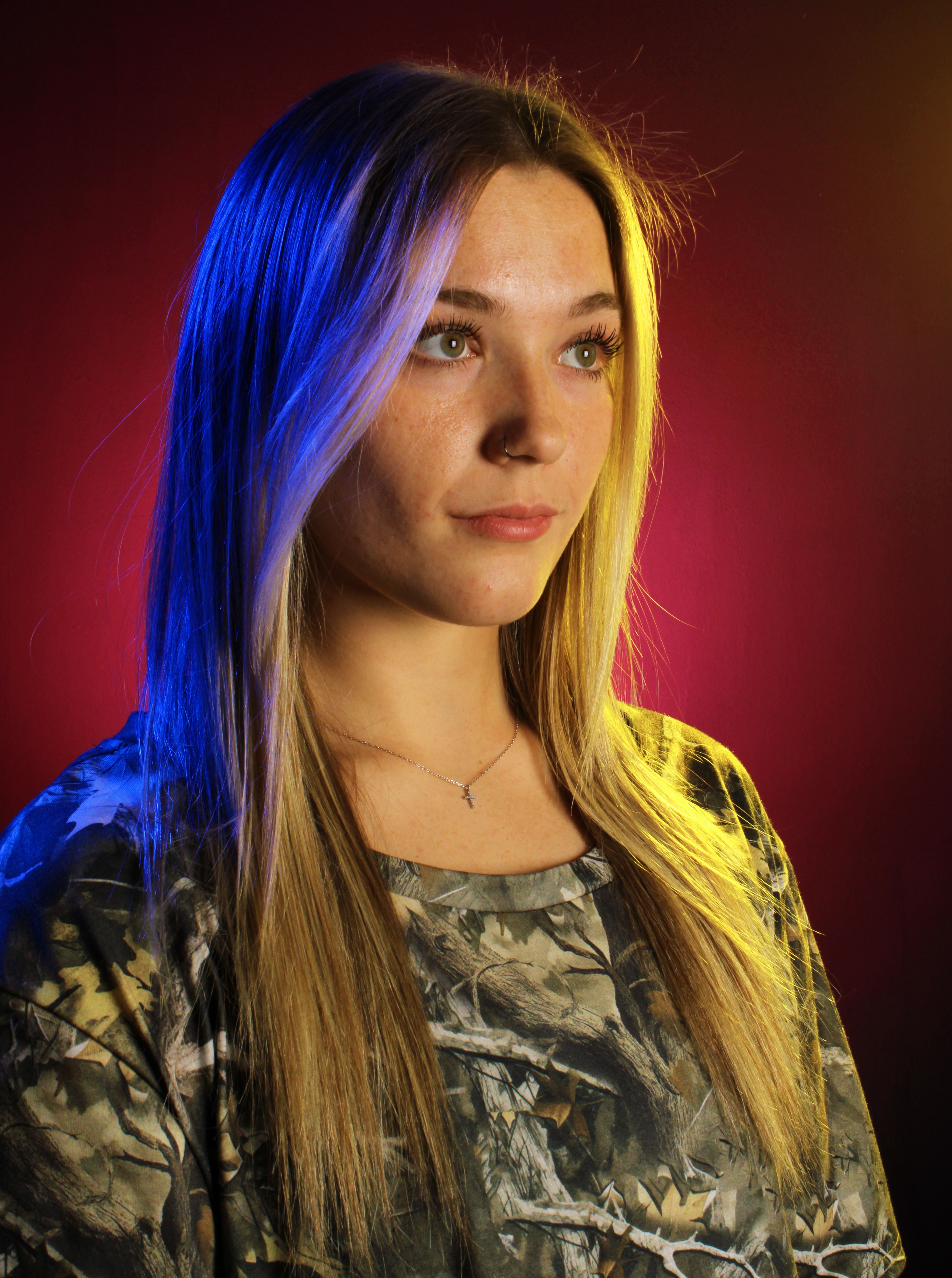 Young woman in camouflage with colorful lighting, creating a dramatic portrait effect.