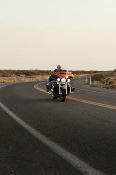 A biker rides a motorcycle along a winding desert road in New Mexico during sunset.
