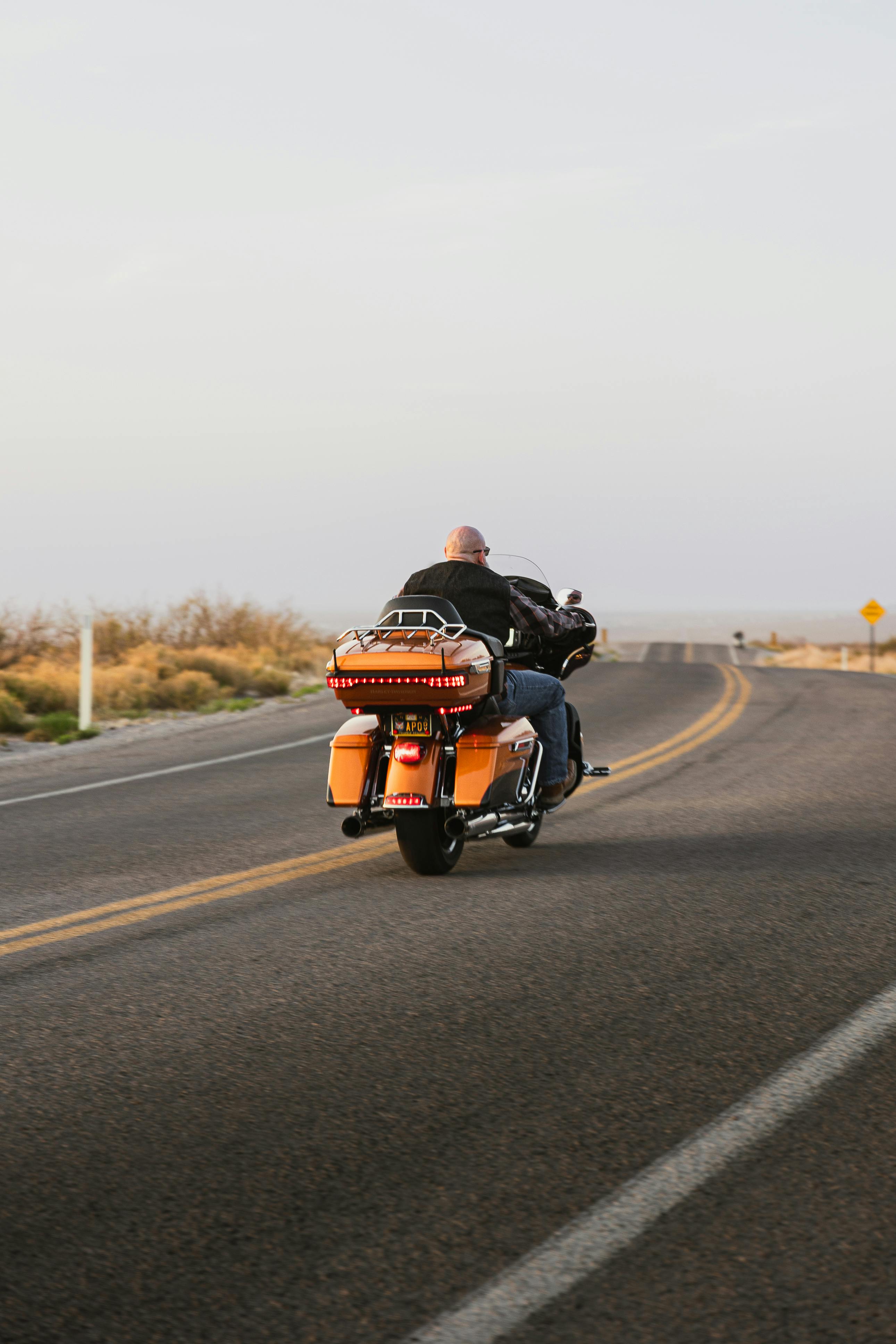 A motorcyclist rides a Harley Davidson down an open, deserted road at sunset in New Mexico.