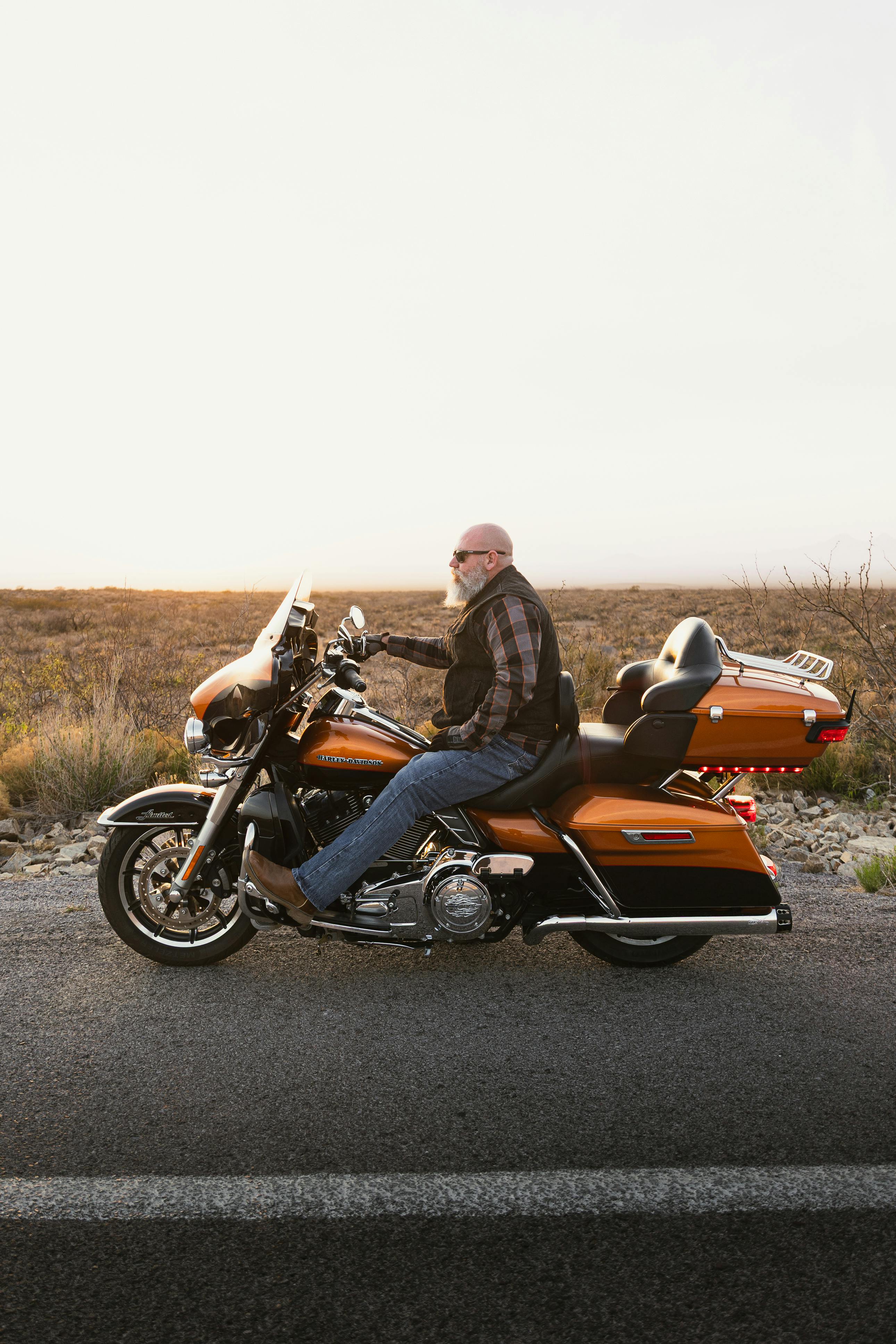 An adult male biker riding a Harley Davidson on a New Mexico roadway during sunset.