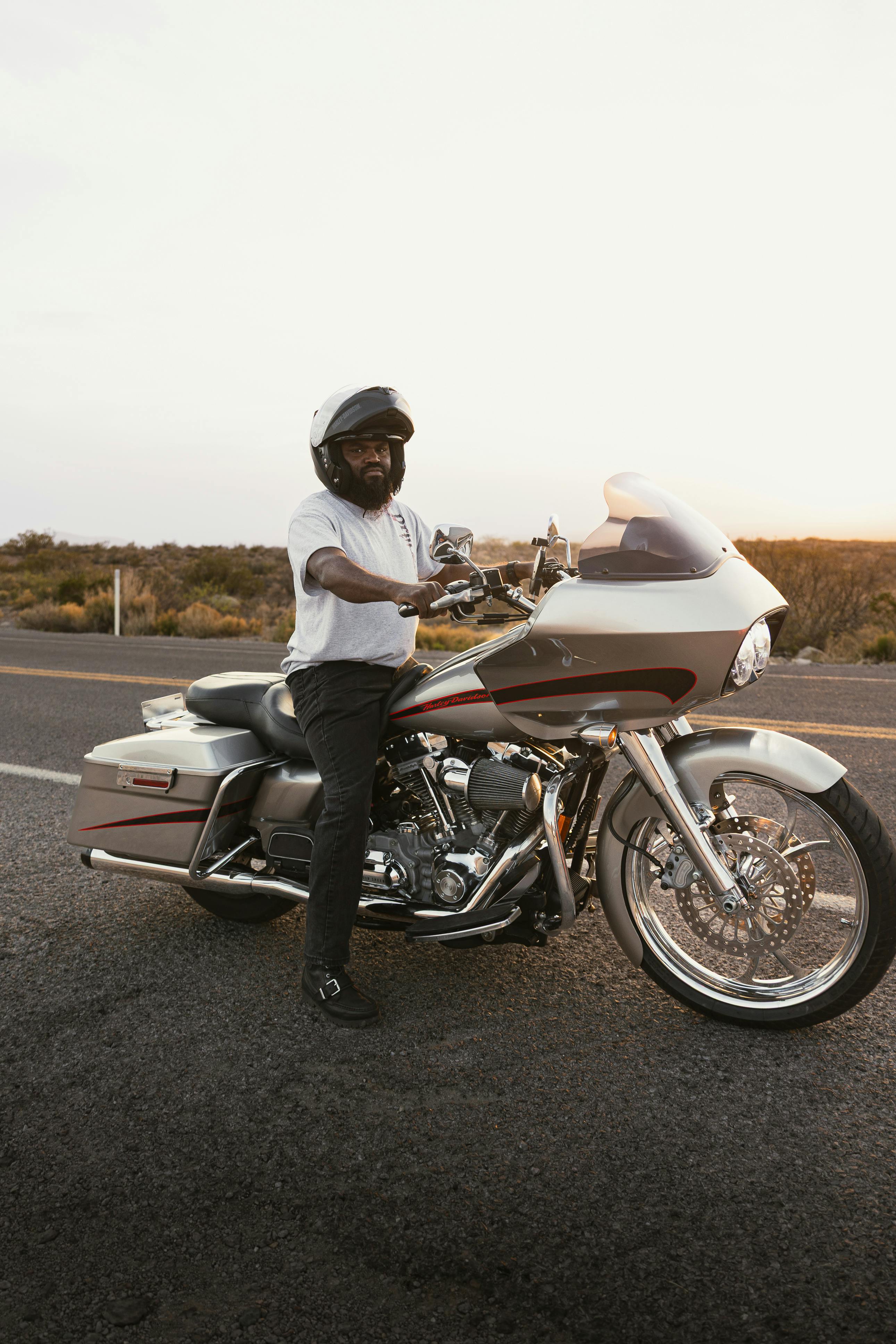 A motorcyclist wearing a helmet stands by his bike on Route 66 in New Mexico during sunset.