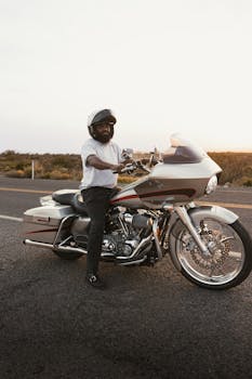 A motorcyclist wearing a helmet stands by his bike on Route 66 in New Mexico during sunset.