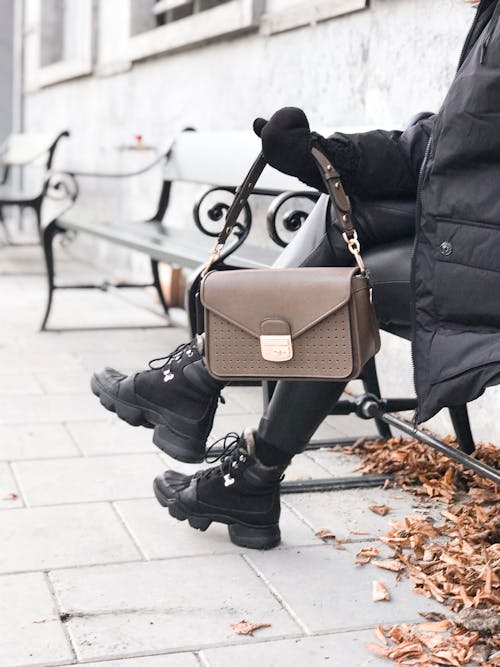 무료 벤치에서 쉬고있는 동안 트렌디 한 손 가방을 보여주는 익명의 여자 스톡 사진