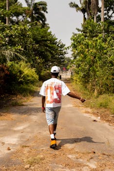 A man walks on a rural path surrounded by lush greenery, capturing a serene, sunny summer day.