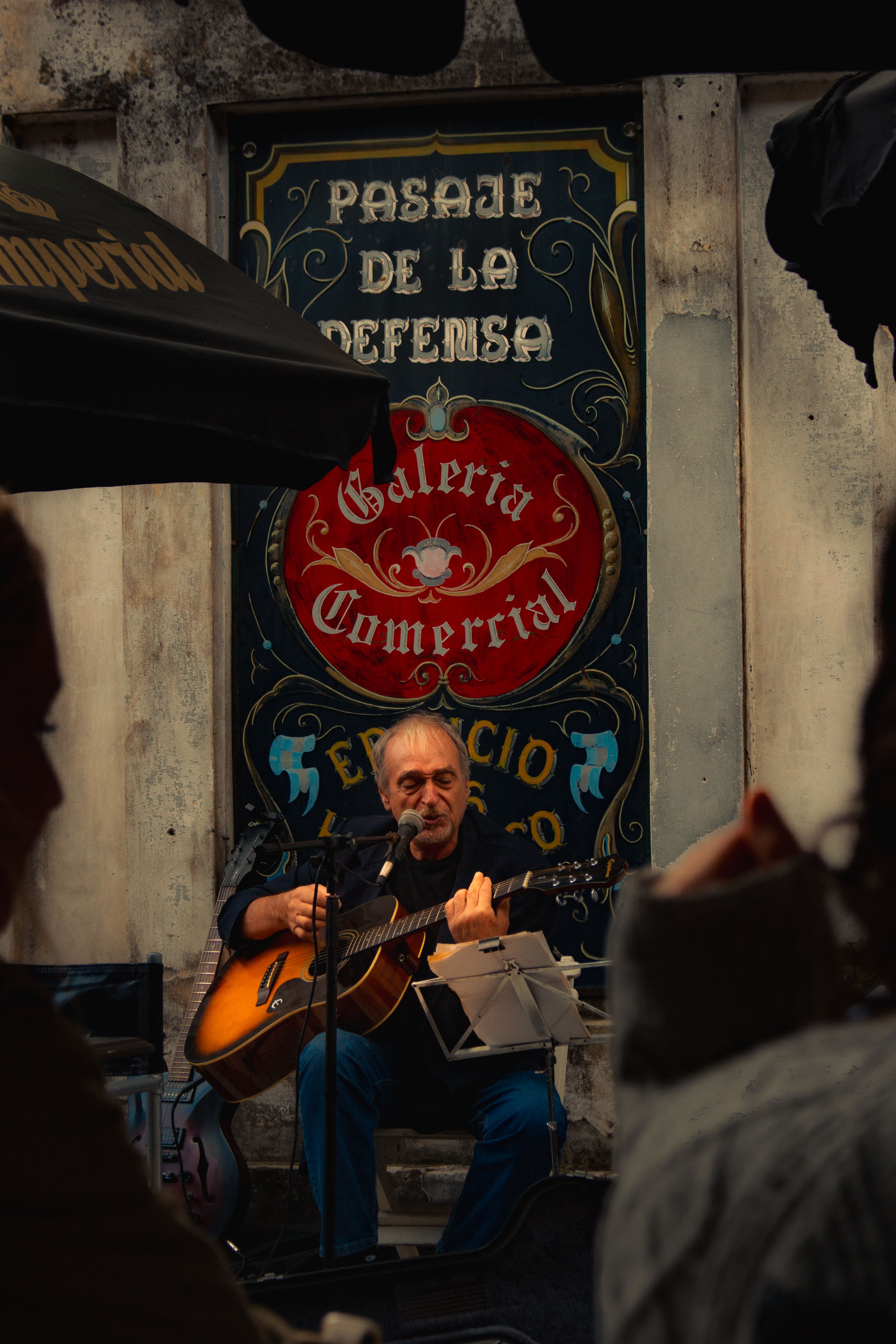 A captivating street musician plays guitar in San Telmo, Buenos Aires, under artistic signage.