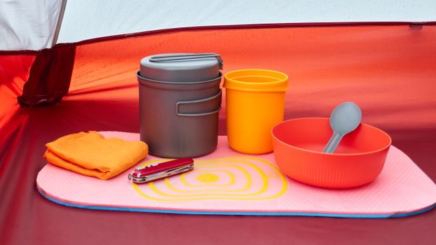 Colorful camping cookware and utensils arranged neatly inside a tent.