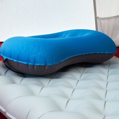 Blue inflatable pillow resting on a grey quilted air mattress inside a tent