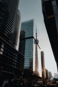 Stunning view of the CN Tower reflection in a glass building amidst Toronto skyscrapers during sunset.