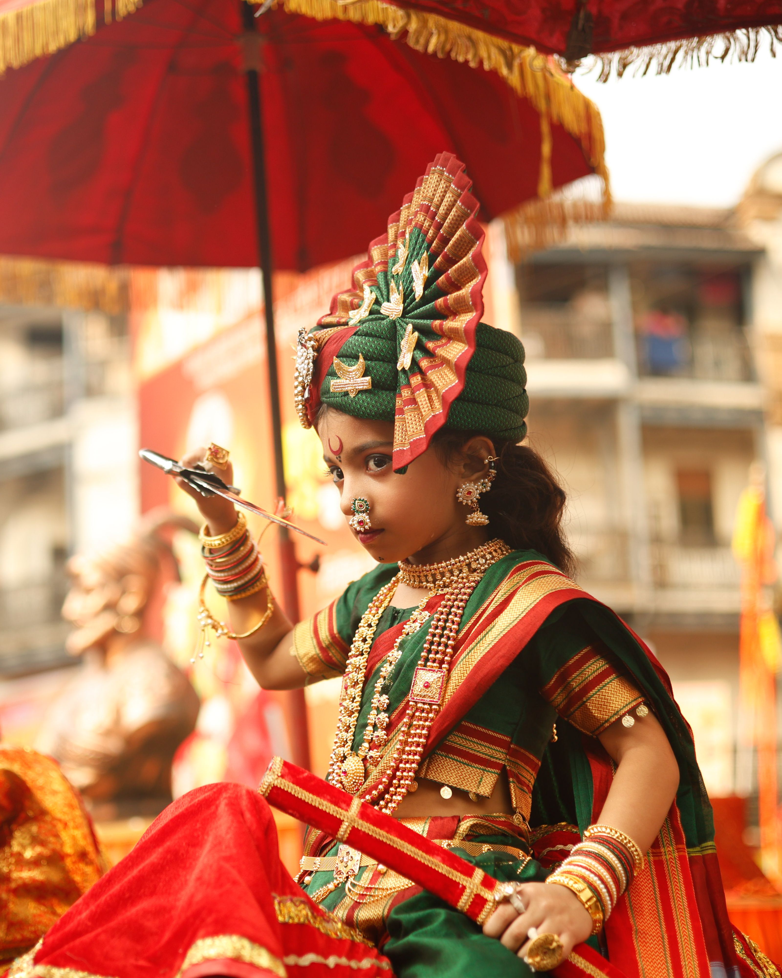 Child dressed in traditional attire under a red canopy at a cultural festival.