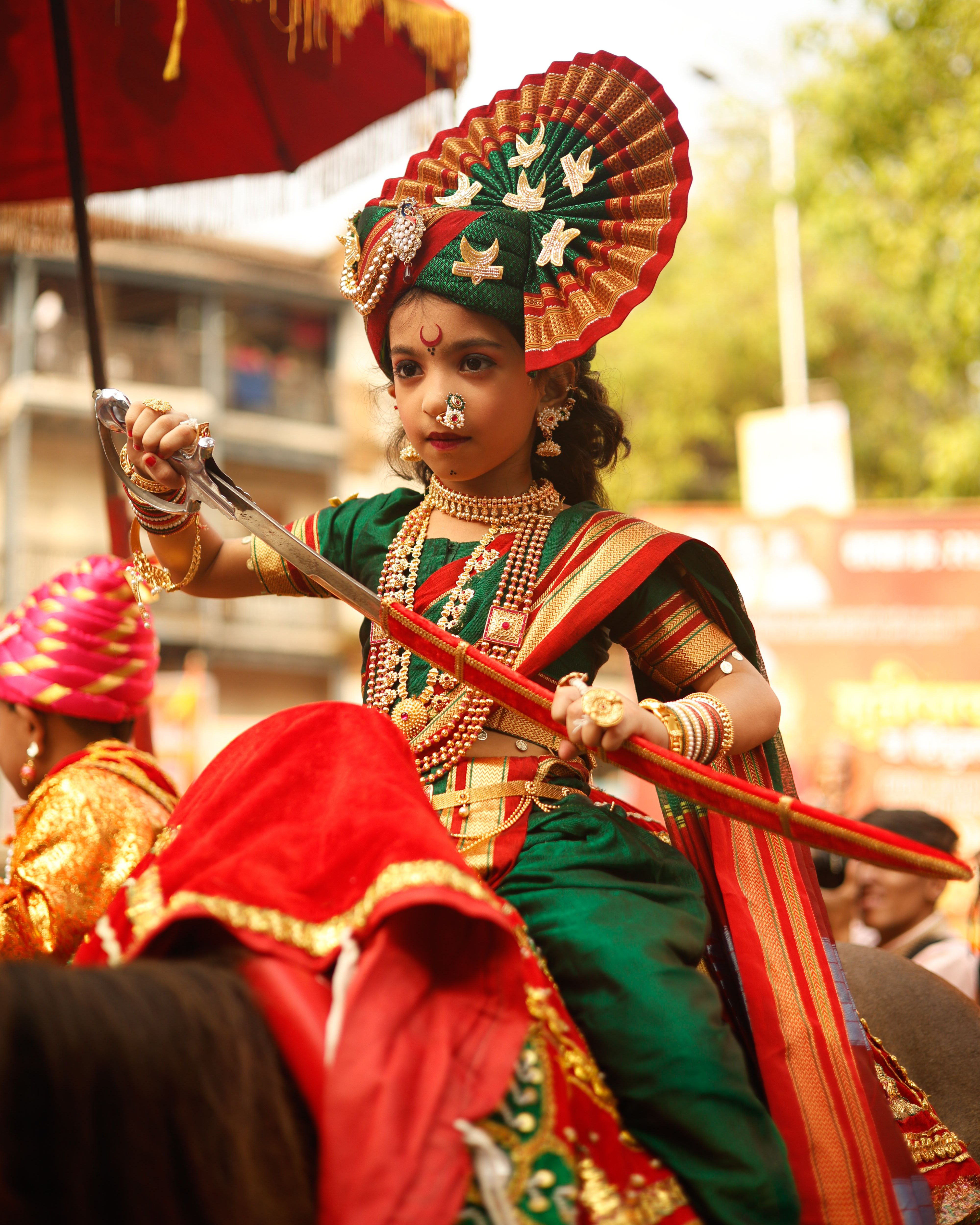 Child in vibrant traditional Indian attire during a lively festival celebration.