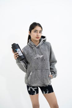 Portrait of a young woman in a hoodie and shorts holding a water bottle, embracing a fitness lifestyle.