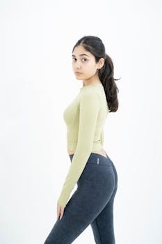 Confident young woman in trendy fitness outfit posing in minimalistic studio setting.
