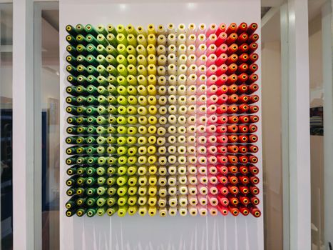 A vibrant wall display of multicolored thread spools creates an artistic pattern indoors.