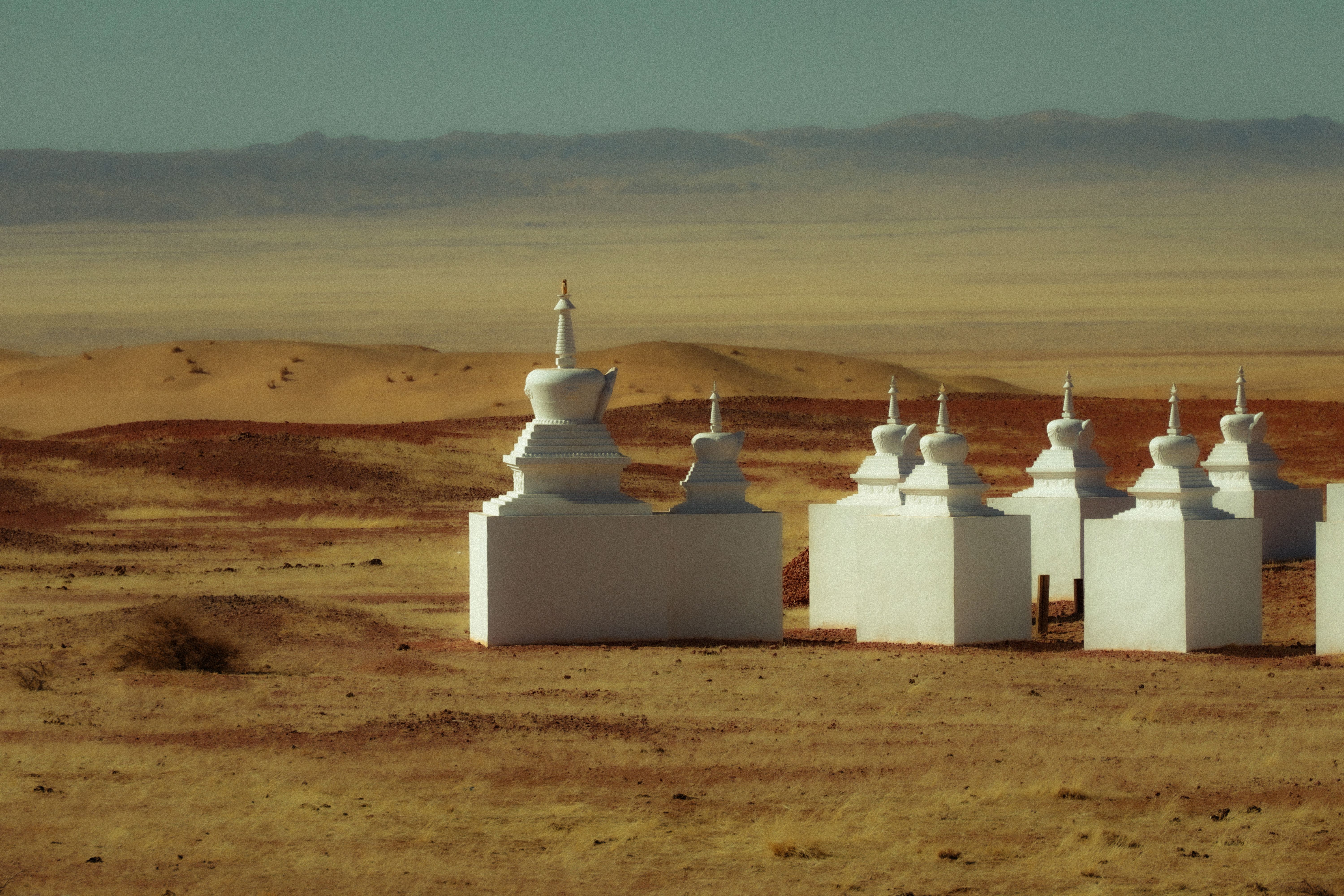 White stupas stand tall in the vast Mongolian desert, under a clear sky, providing a serene view.