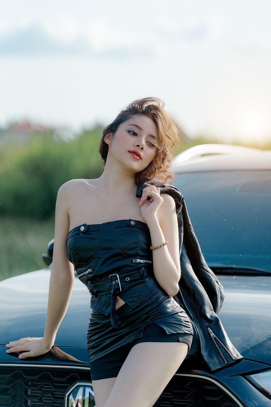 Elegant woman in black outfit posing by car outdoors. Ideal for fashion and lifestyle themes.
