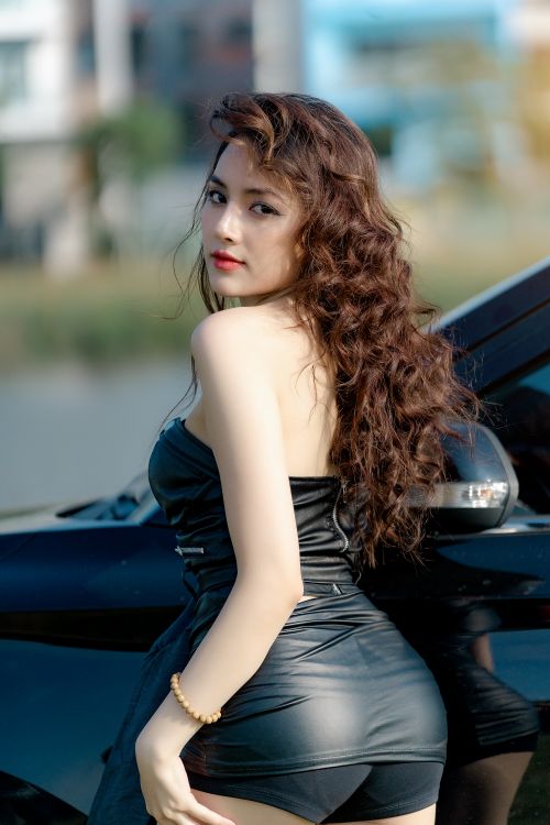 Free Confident woman in black attire poses beside a sleek car on a sunny day. Stock Photo