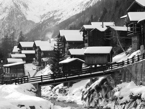 Black and white photo of an Alpine village with snow-covered cabins and mountains.