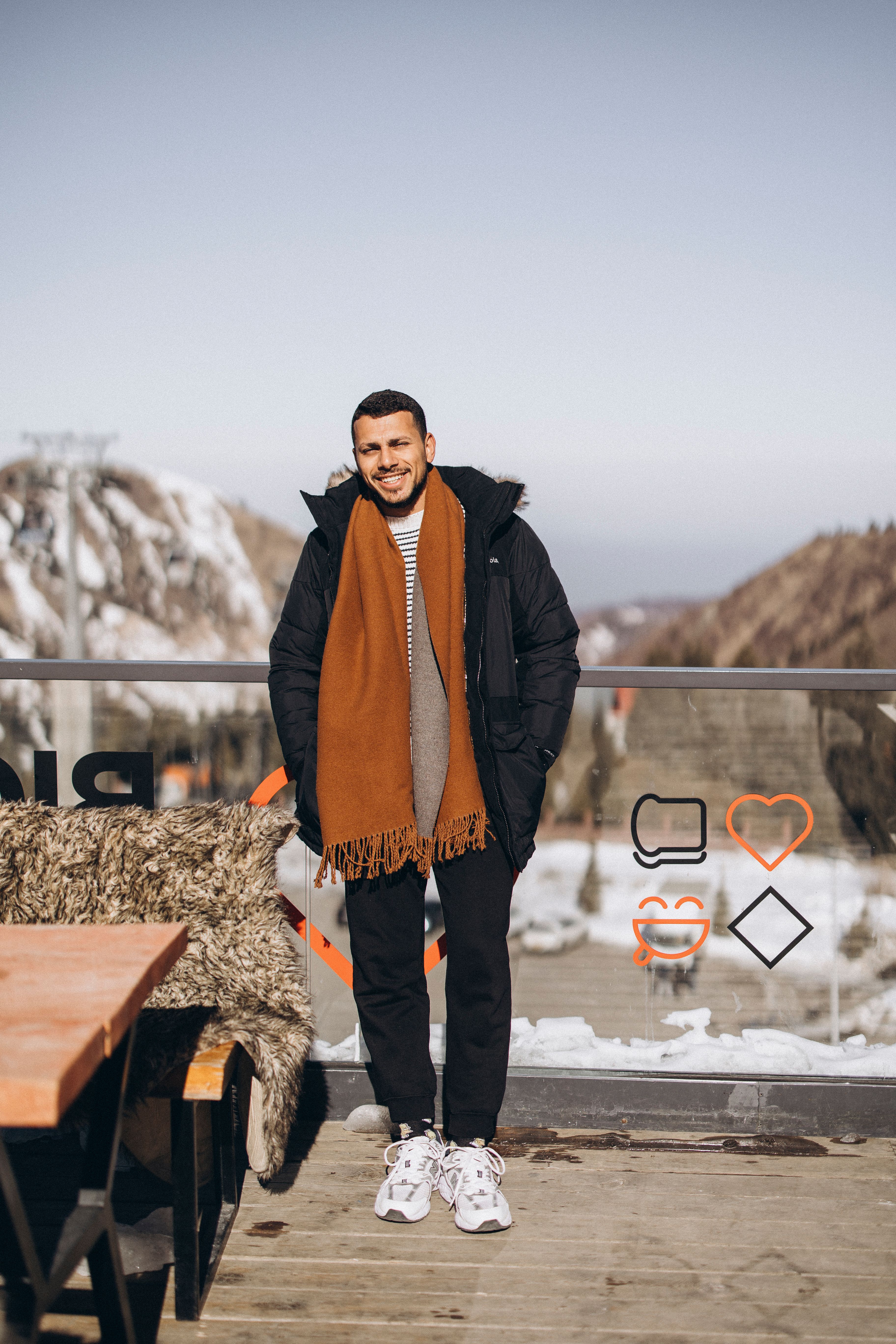 A stylish man in winter attire enjoying a scenic view of snow-covered mountains in Almaty, Kazakhstan.