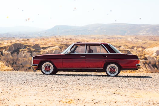 Vintage red Mercedes car with hot air balloons in Cappadocia, Turkey, showcasing stunning landscape.